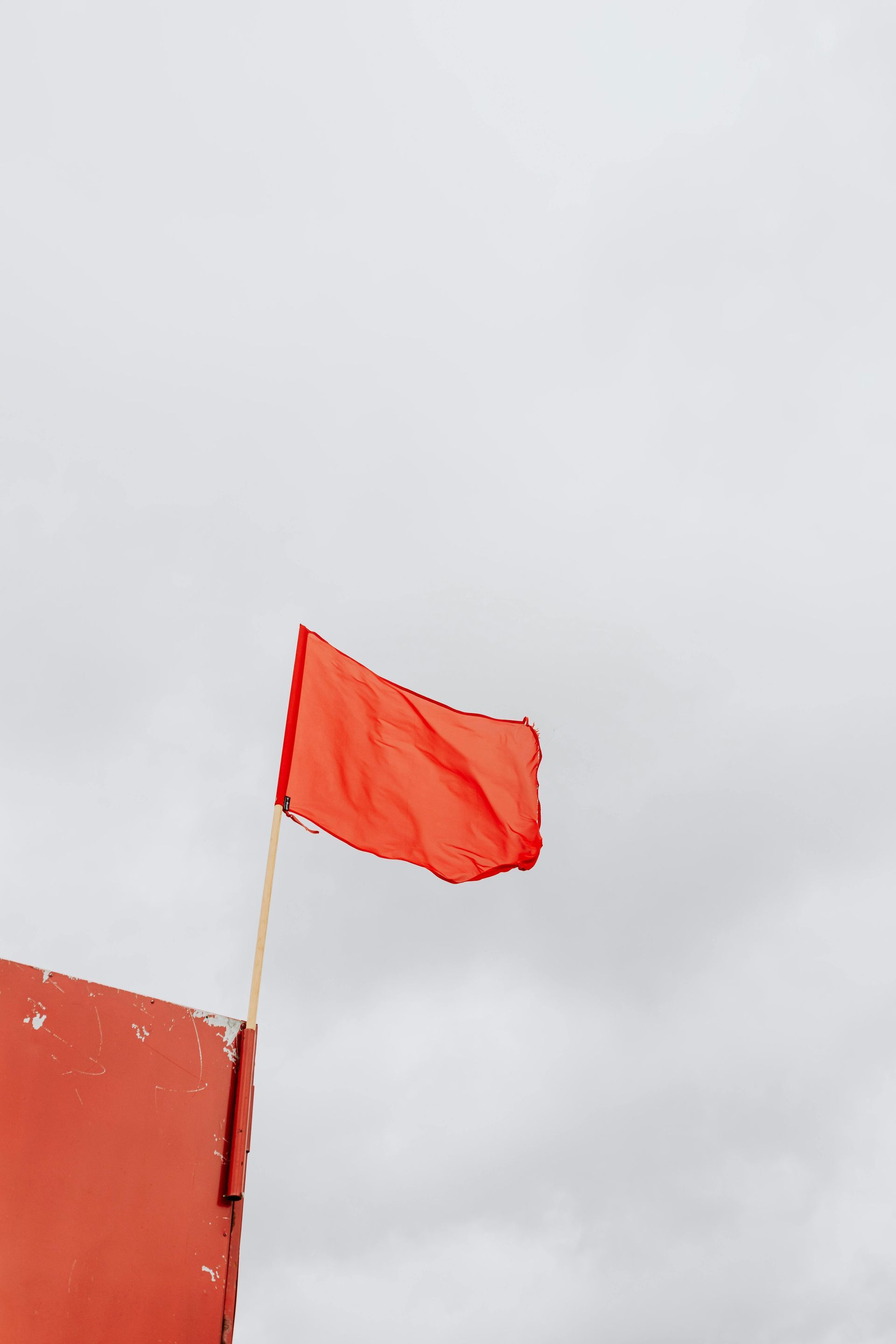 A red flag atop a building with an eerie, cloudy sky in the background.
