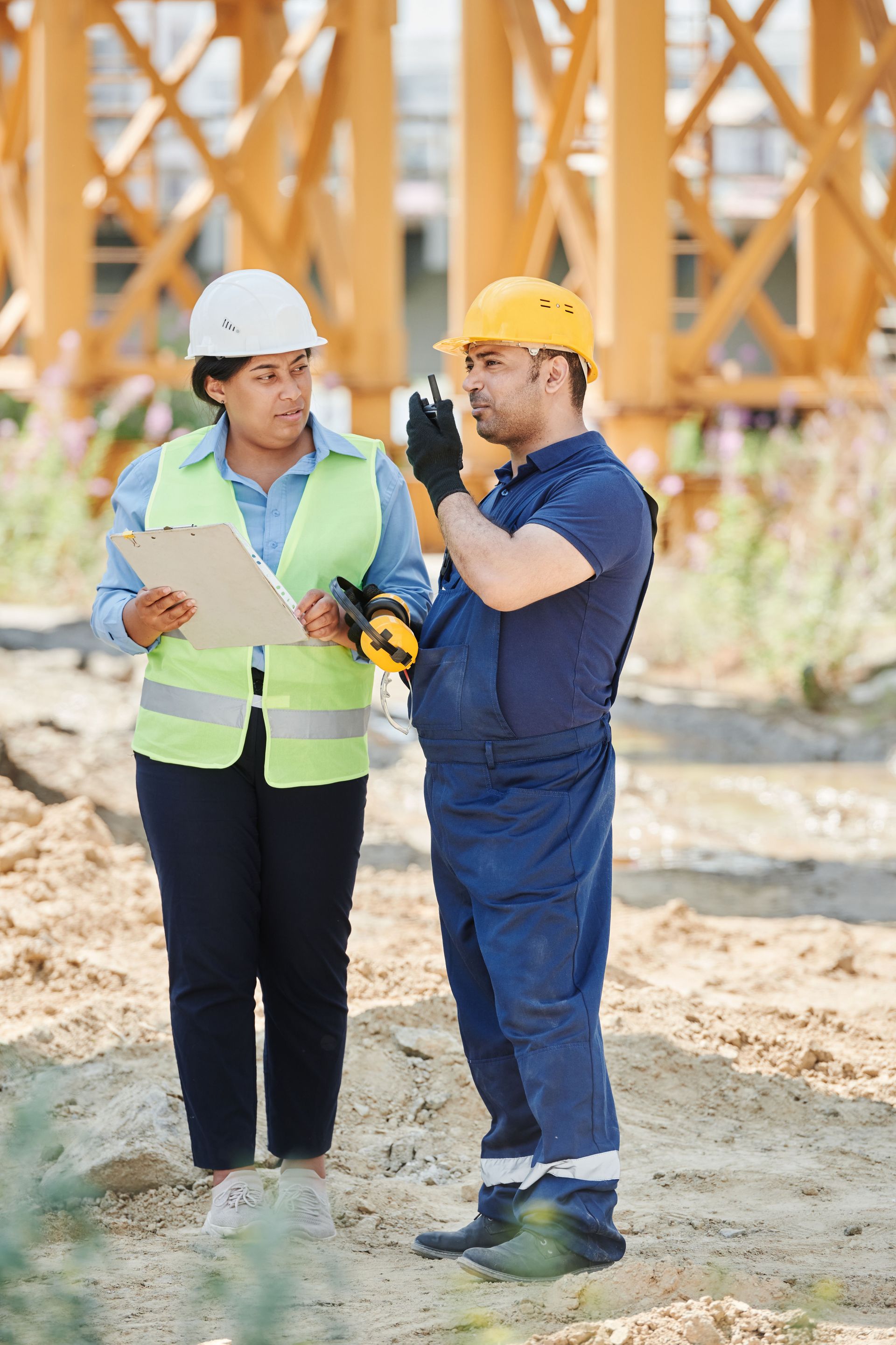Two workers in hard hats discussing plans at a construction site.