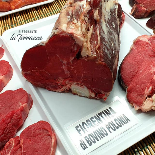 Una grande bistecca cruda alla fiorentina di manzo polacco esposta in una vetrina insieme ad altri tagli.