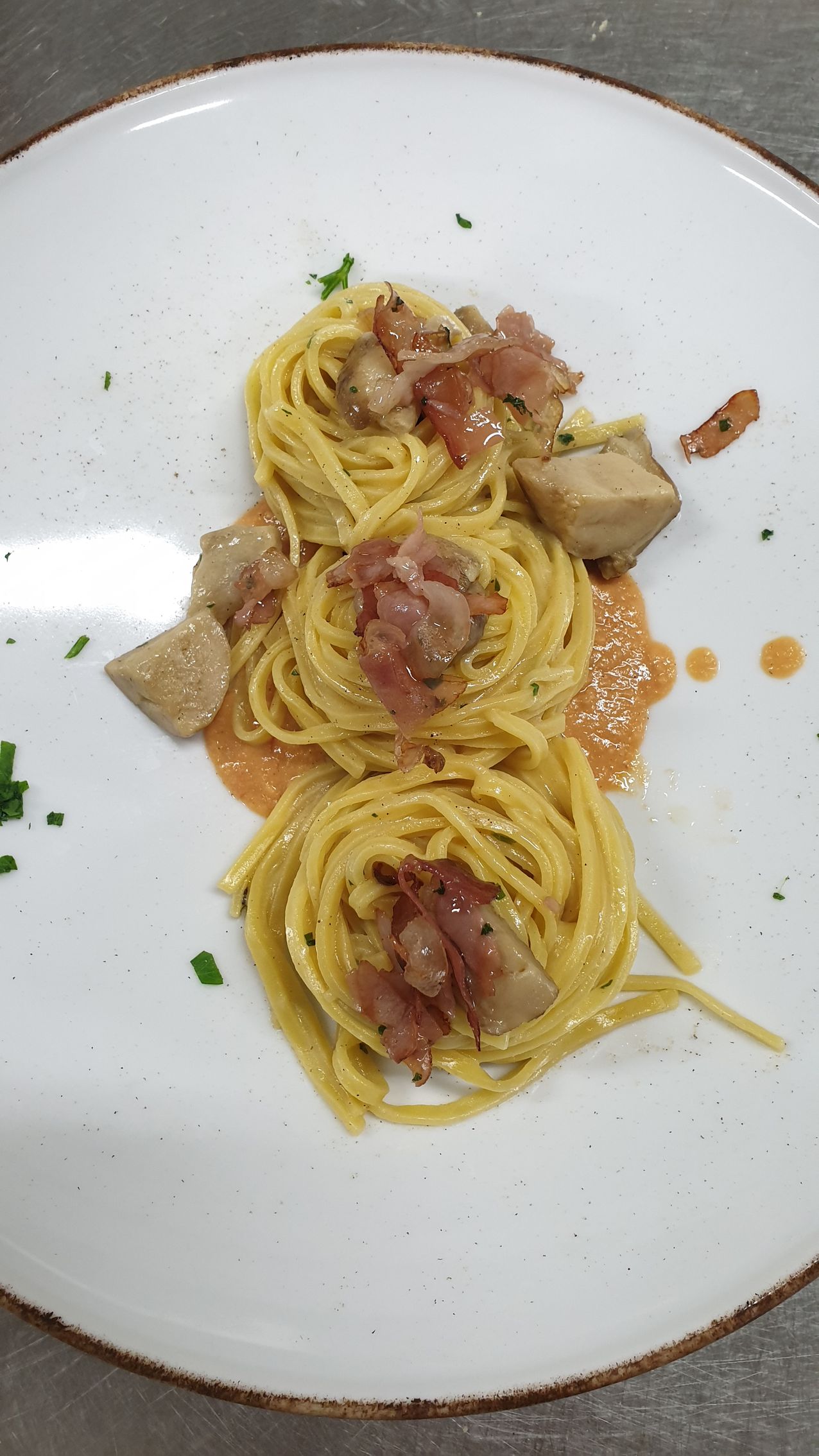 Nidi di pasta conditi con pancetta e funghi, serviti su un piatto bianco.