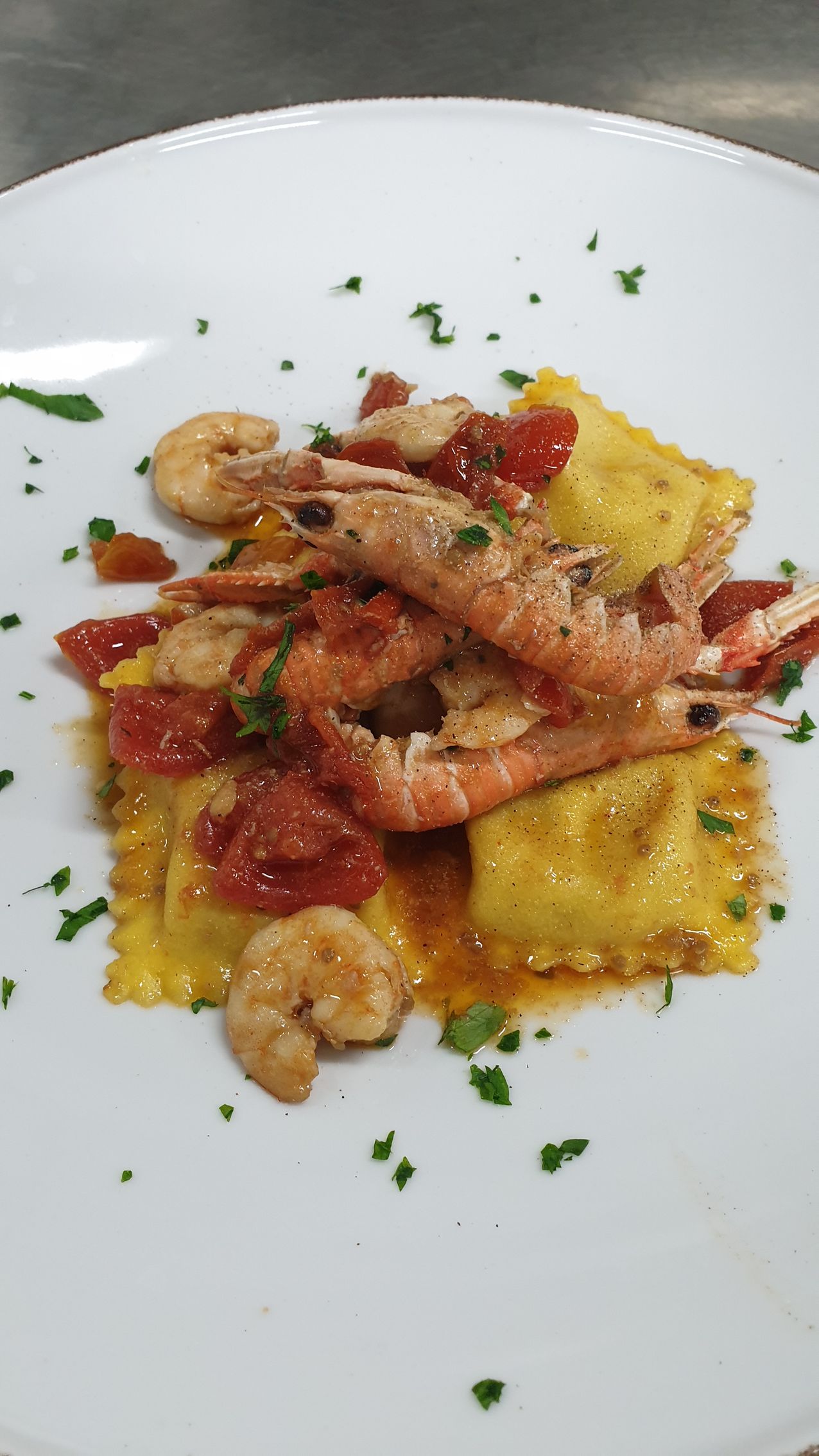 Ravioli con gamberi e pomodori a cubetti, guarniti con prezzemolo, serviti su un piatto bianco.