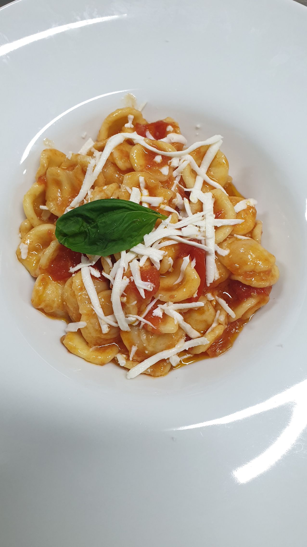 Piatto di pasta con salsa di pomodoro, formaggio e basilico su un piatto bianco.