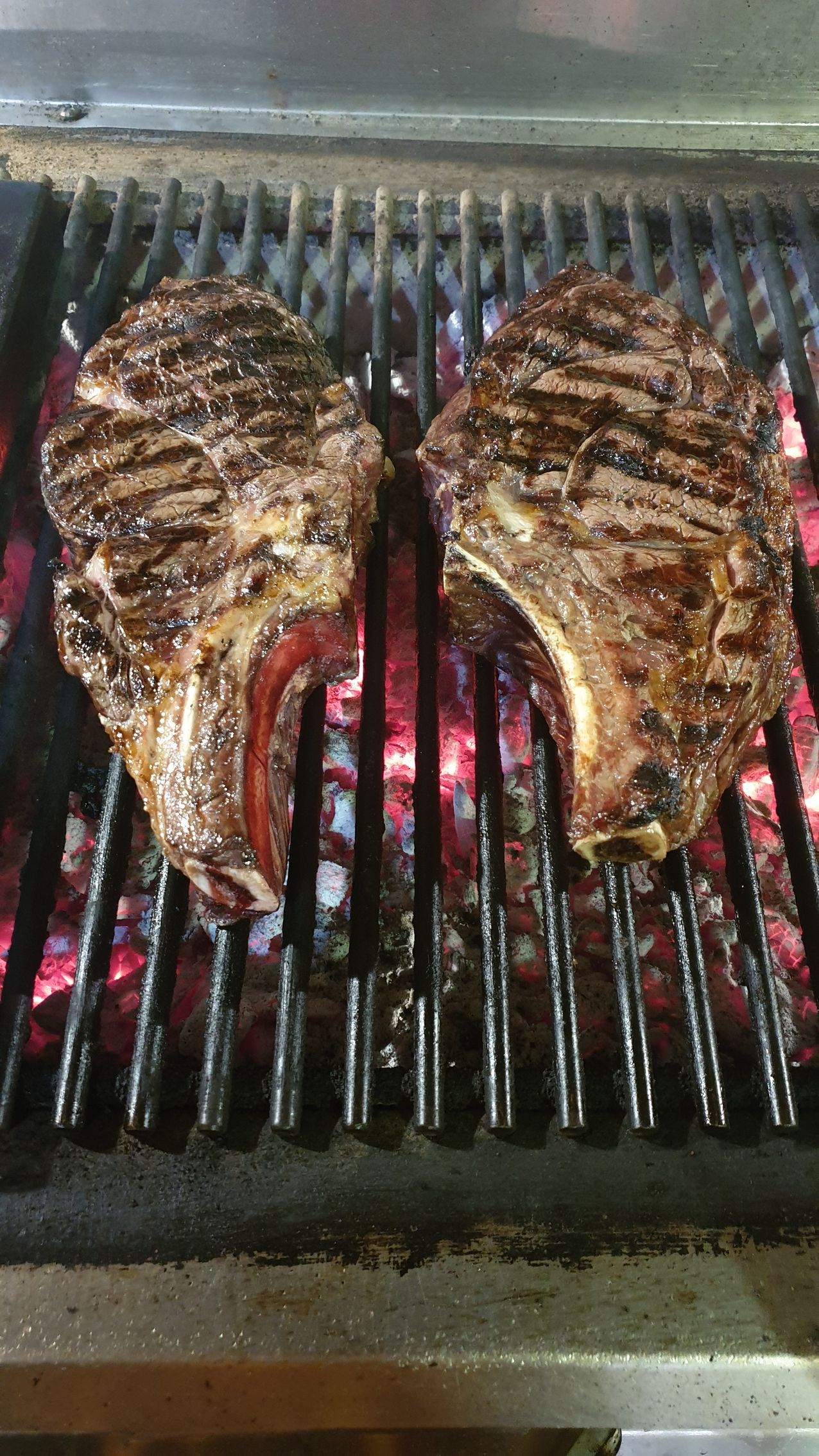 Due bistecche di ribeye spesse e scottate, cotte su una griglia a carbone bollente.