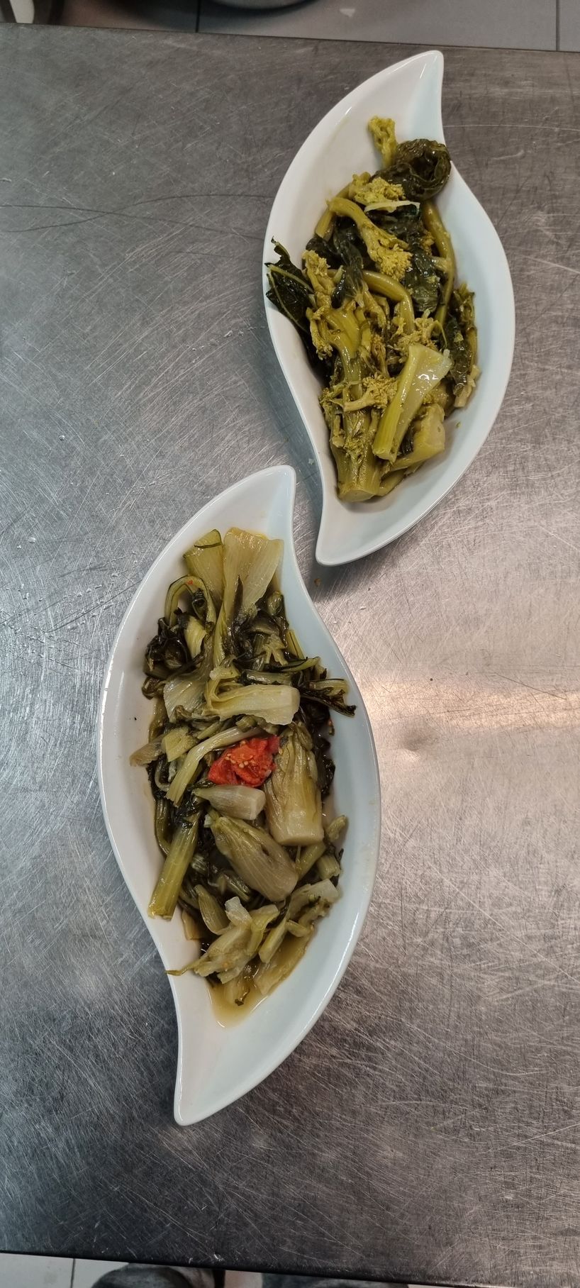 Due piatti bianchi a forma di foglia con verdure cotte su una superficie metallica.