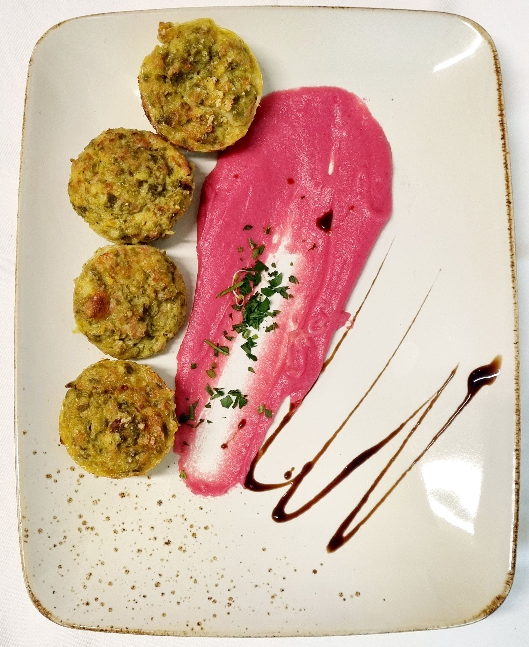 Quattro tortini vegetariani dorati con una salsa rosa acceso e glassa balsamica su un piatto bianco.