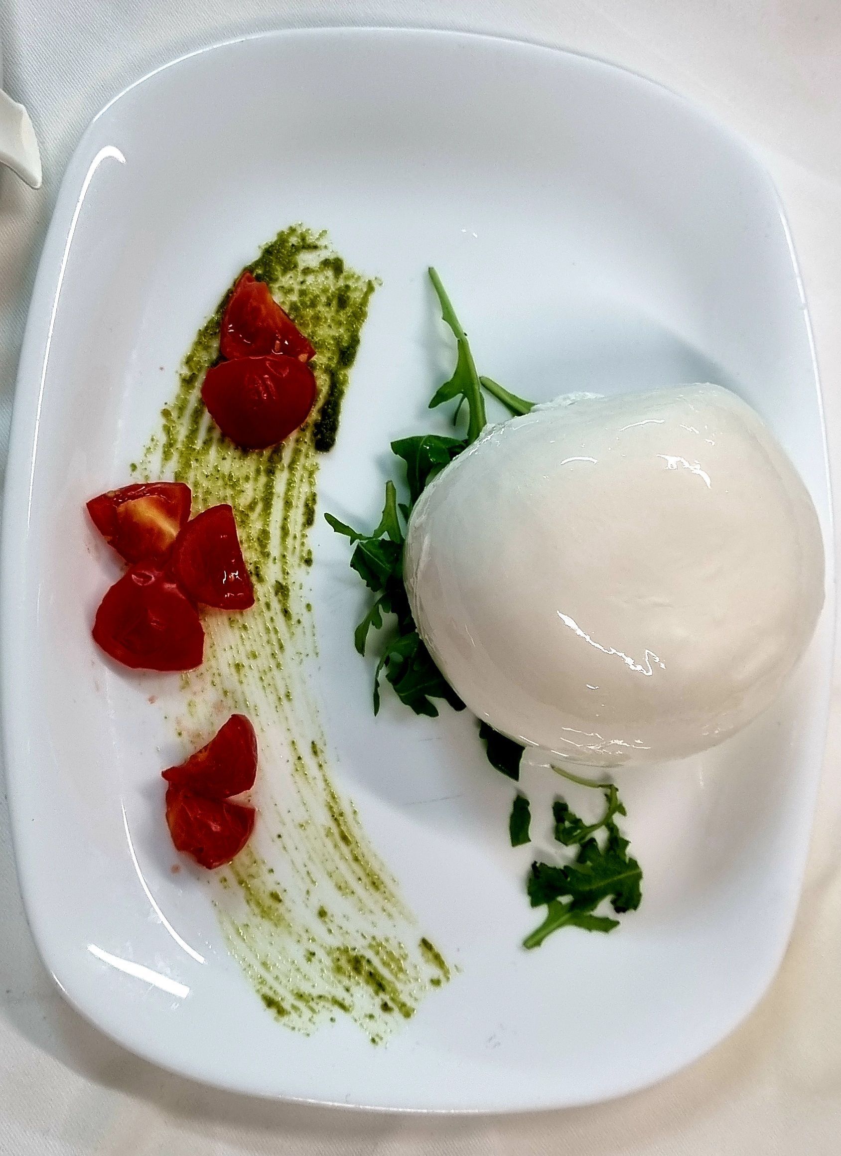 Piatto bianco con mozzarella, pesto, pomodori e rucola.