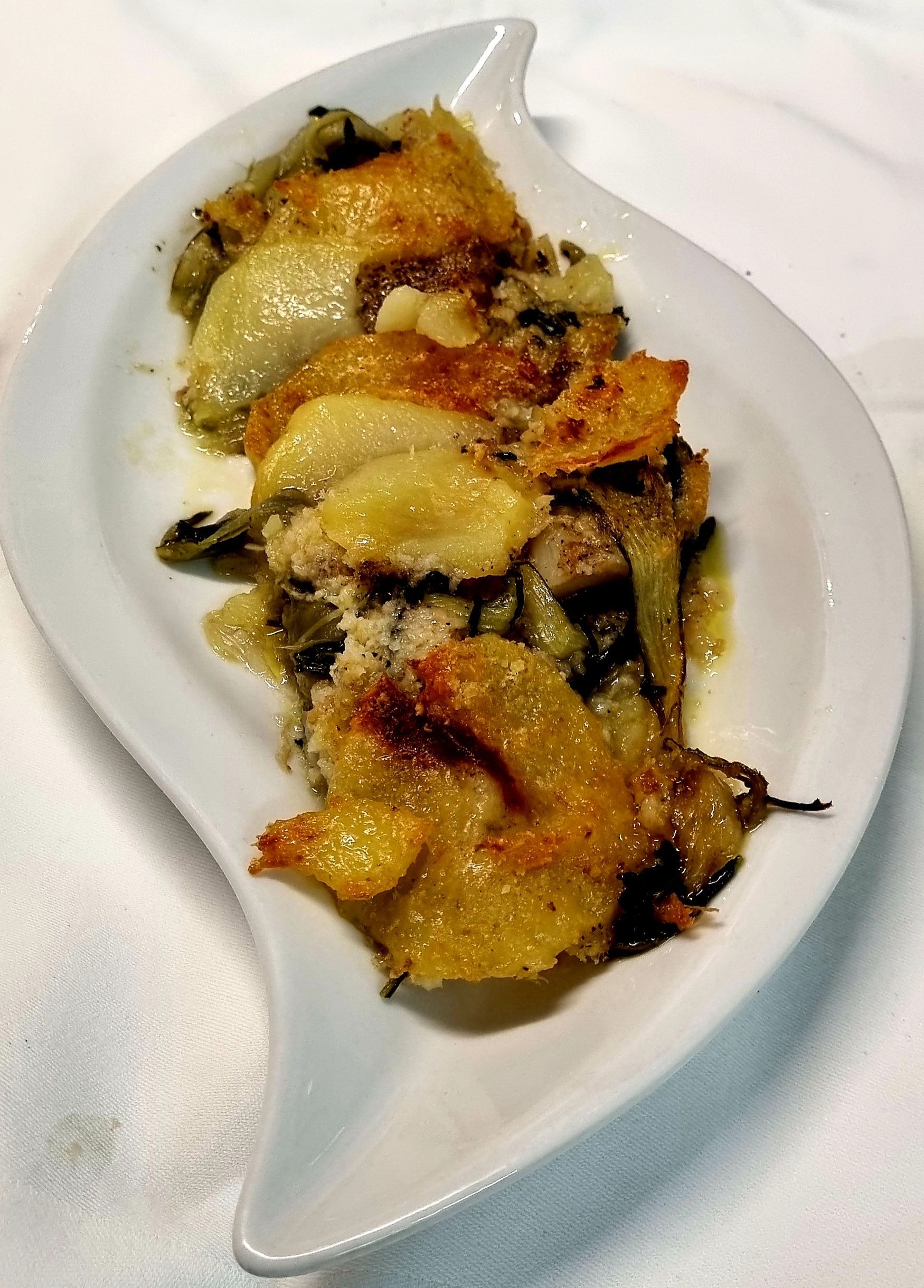 Piatto cotto al forno su un piatto bianco a forma di foglia. Crosta dorata in superficie con verdure e salsa a vista.