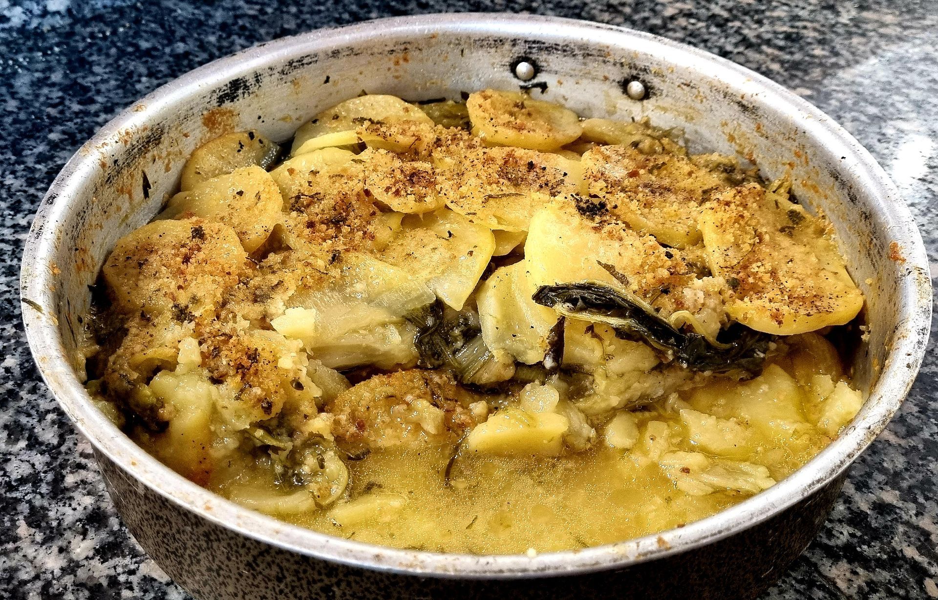 Piatto di patate e pesce al forno in una padella di metallo.