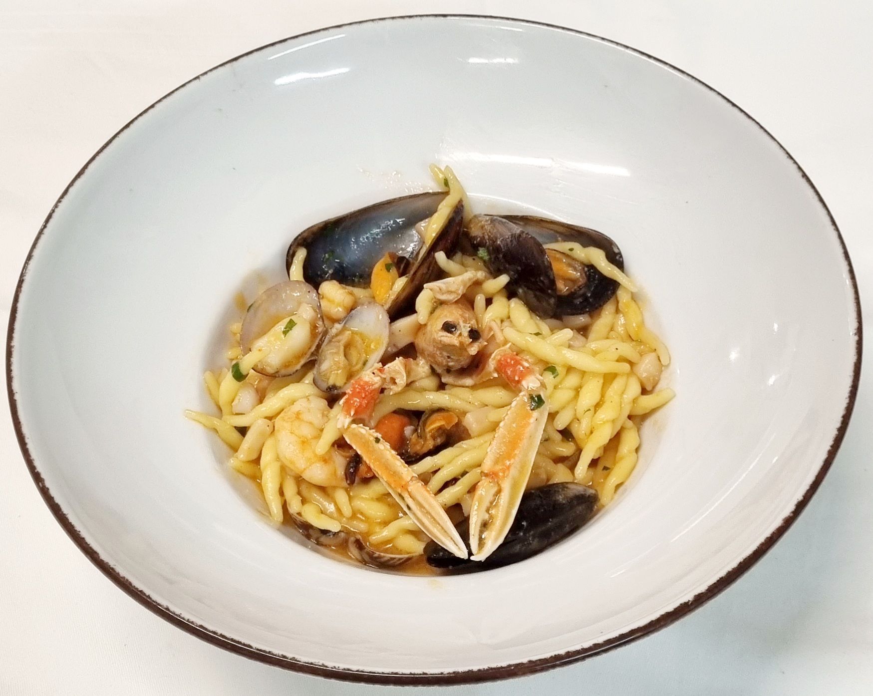 Piatto di pasta con frutti di mare in una ciotola bianca: cozze, vongole, gamberi ed erbe aromatiche.