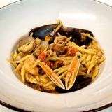 Pasta con frutti di mare, tra cui gamberi, cozze e chele di granchio, in una ciotola bianca.