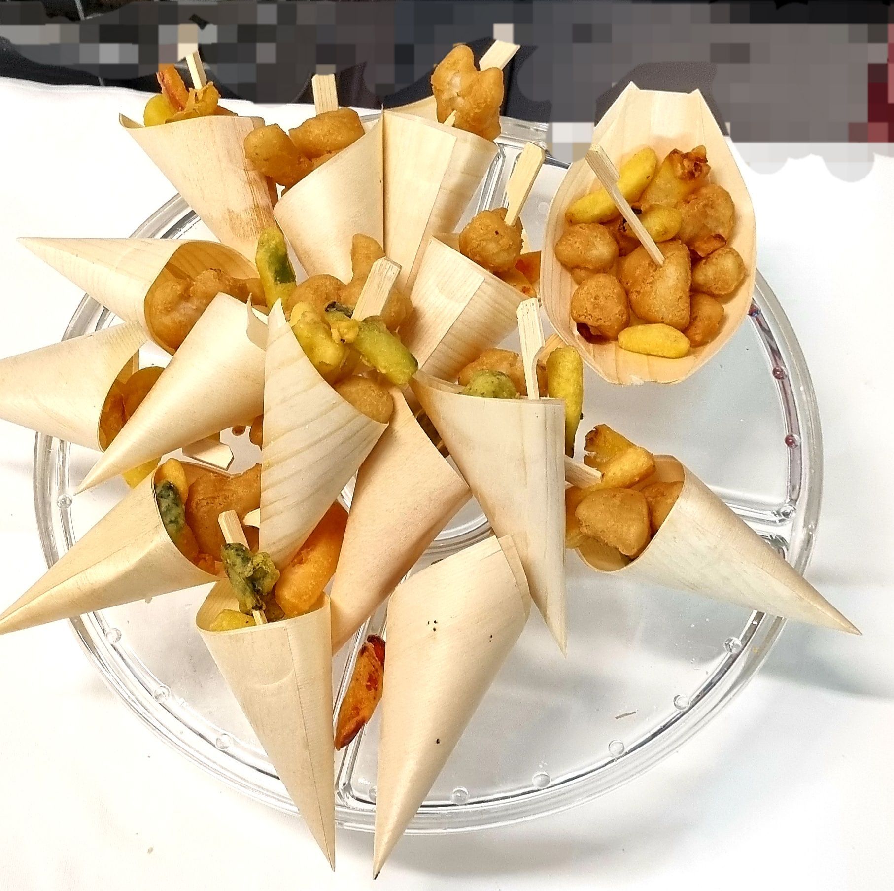 Antipasti in coni di legno su un piatto trasparente; alcuni con spiedini.