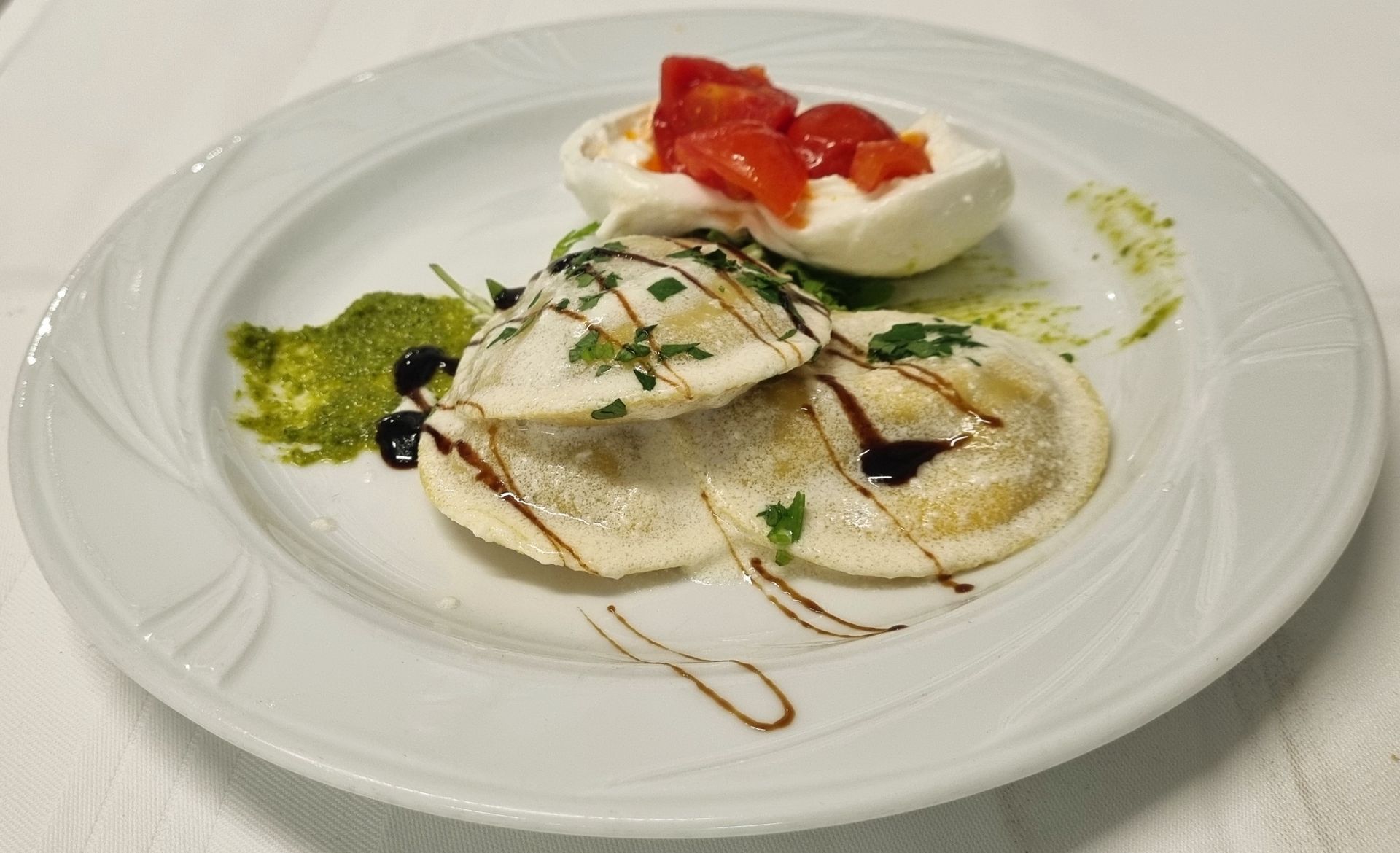 Piatto di ravioli con mozzarella e pomodori, conditi con glassa balsamica e pesto.