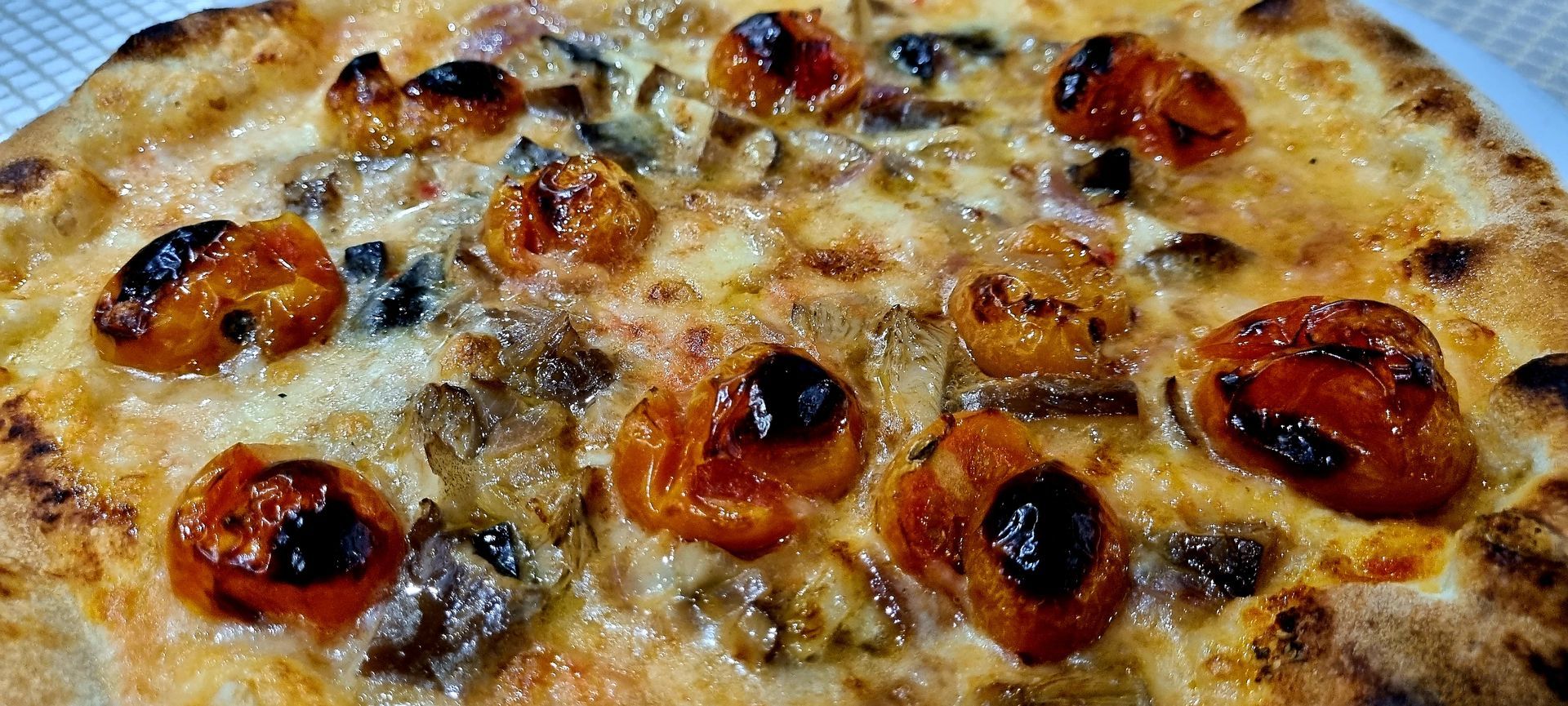 Primo piano di una pizza condita con pomodori, formaggio e funghi. La crosta è dorata.