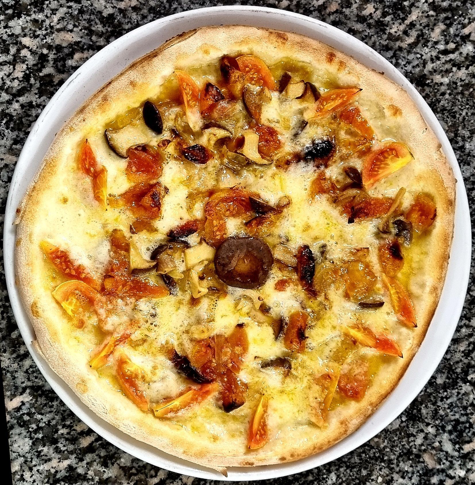 Pizza condita con pomodori, funghi e formaggio su un piatto bianco.