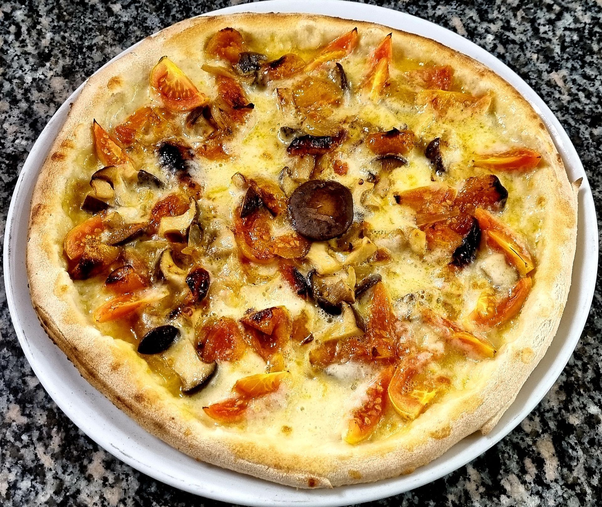 Pizza con funghi e pomodori su un piatto bianco.