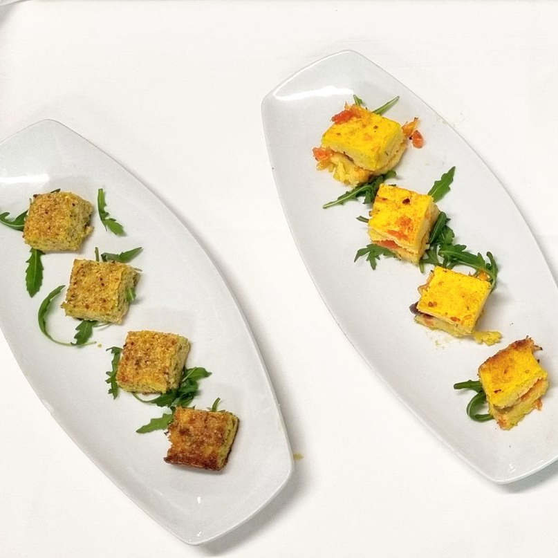 Due piatti bianchi con antipasti: quadrato e rotondo, su rucola.