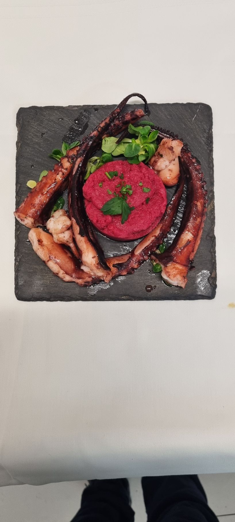 Polpo alla griglia con tartare di barbabietola rosa su un piatto quadrato scuro.