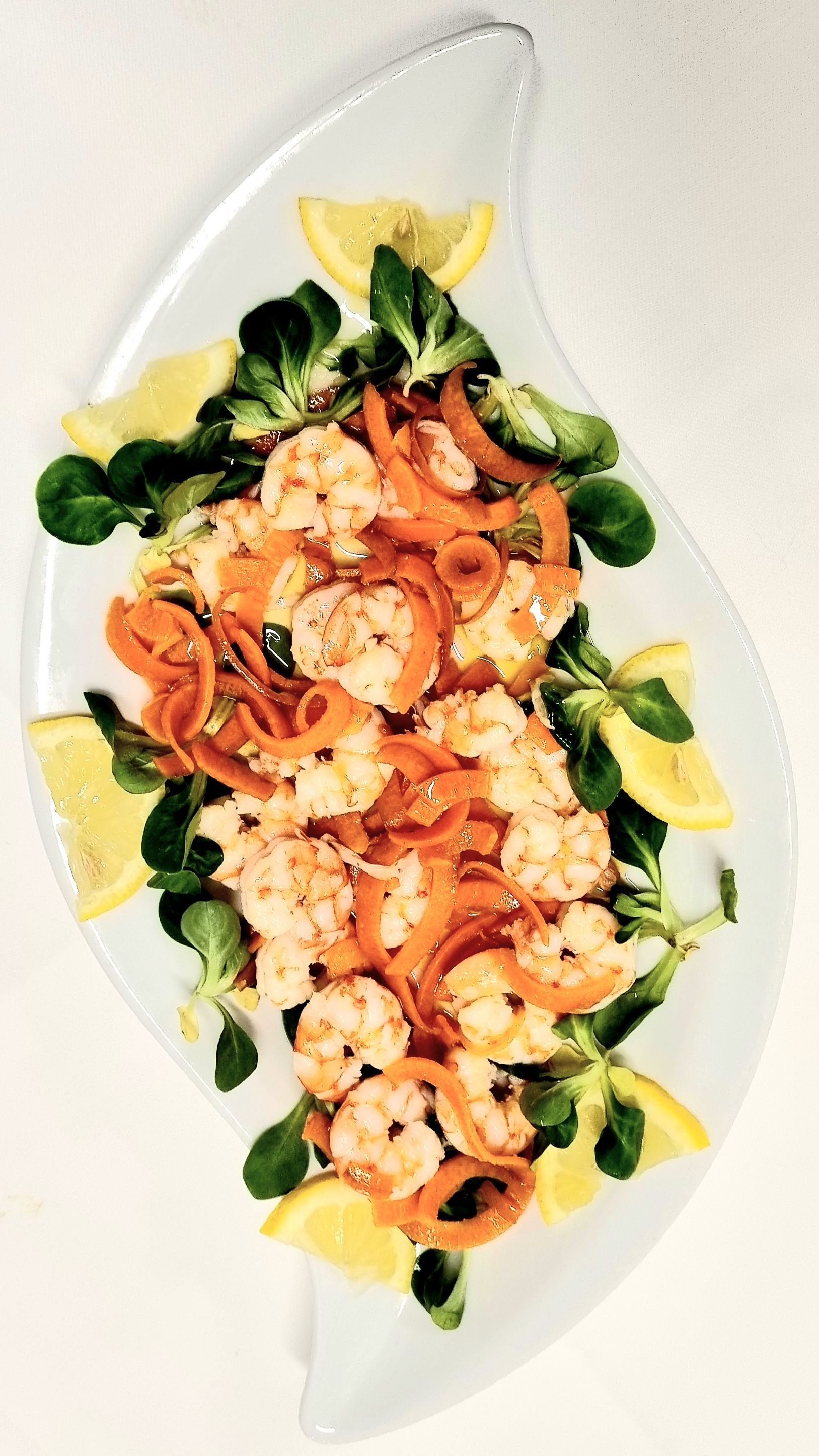 Insalata di gamberi con carote, verdure e spicchi di limone su un piatto bianco a forma di foglia.