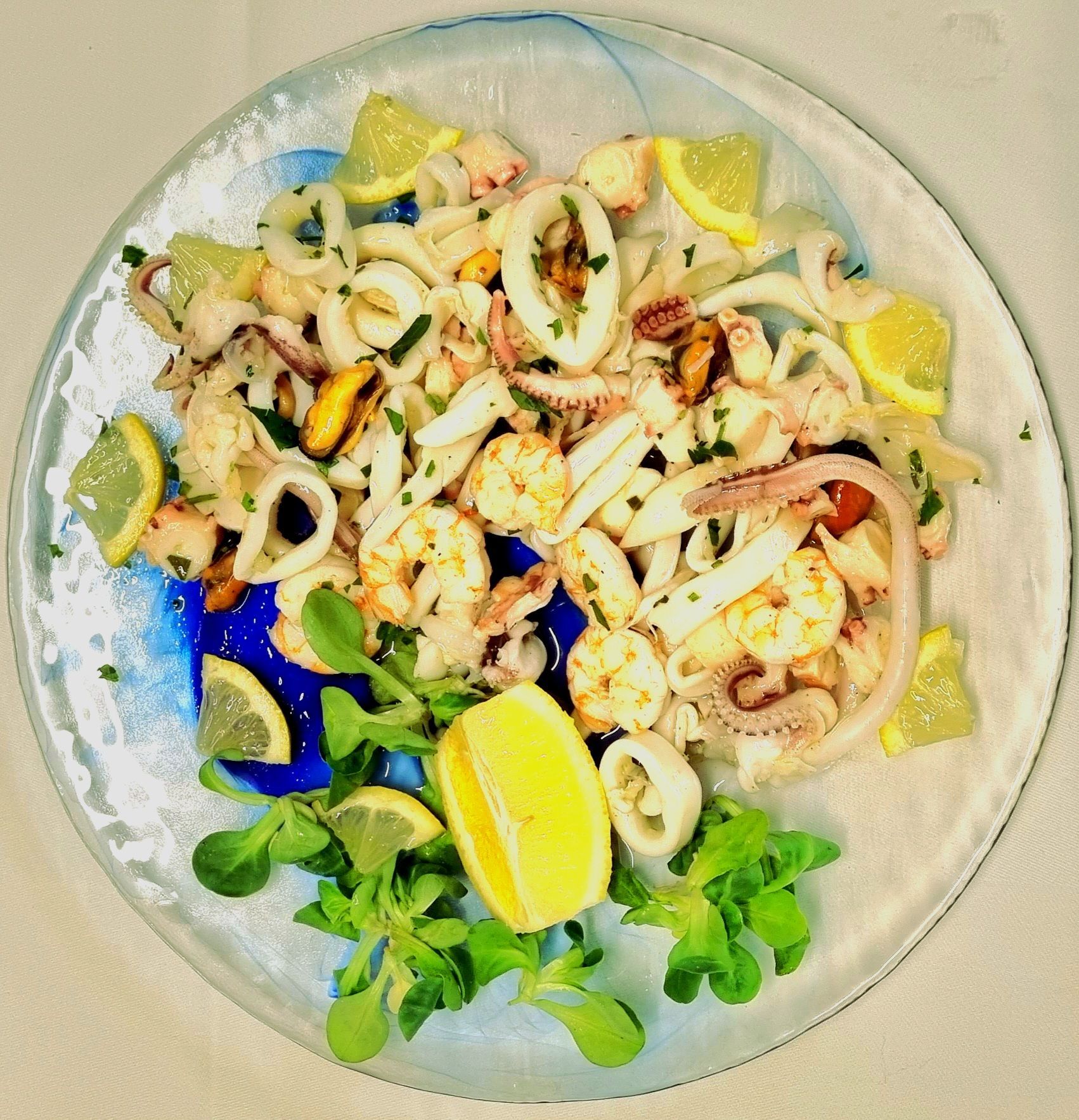 Insalata di mare con fette di limone e verdure su un piatto di vetro.