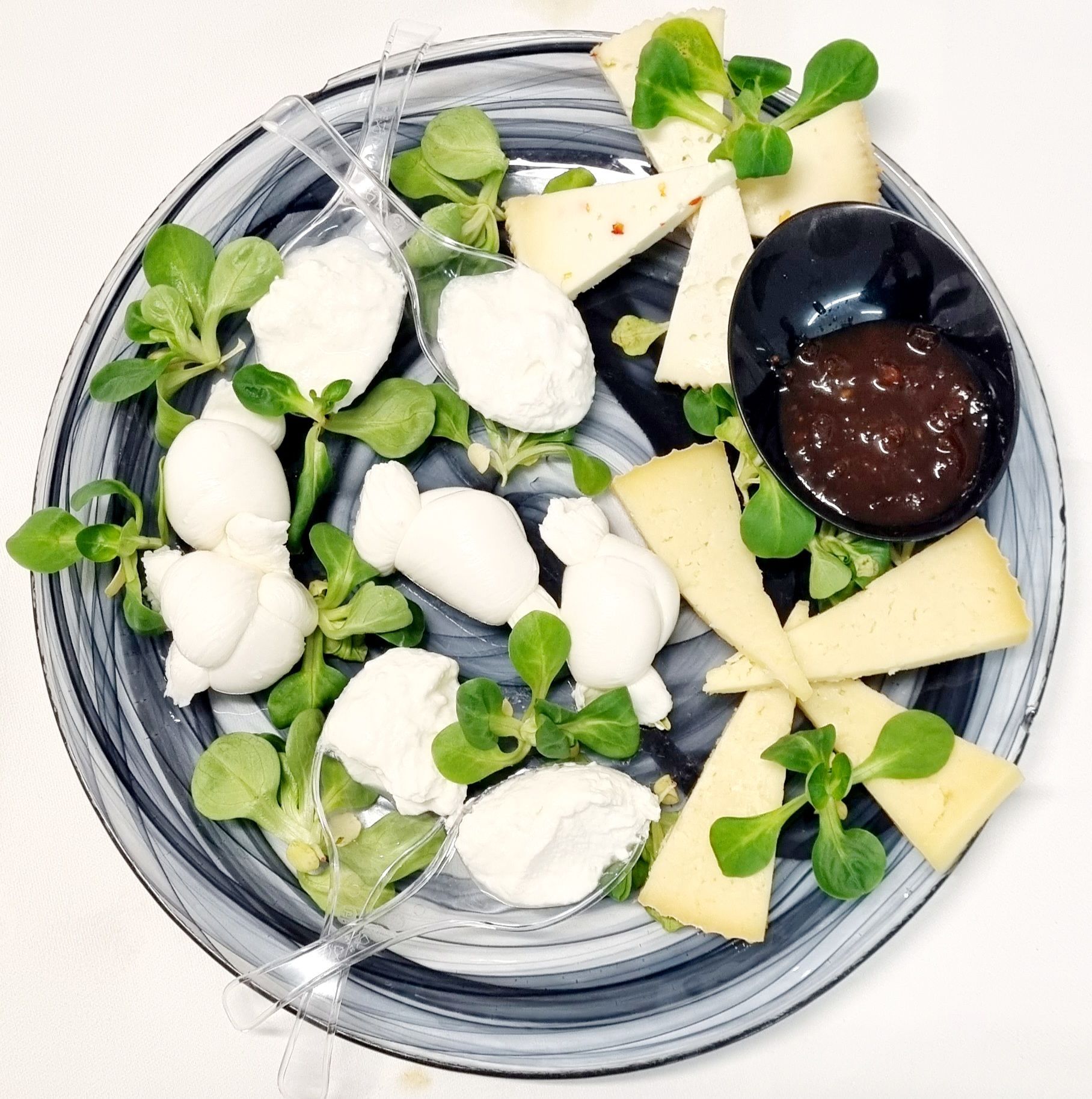 Antipasto di formaggio e marmellata su un piatto decorato, guarnito con verdure.