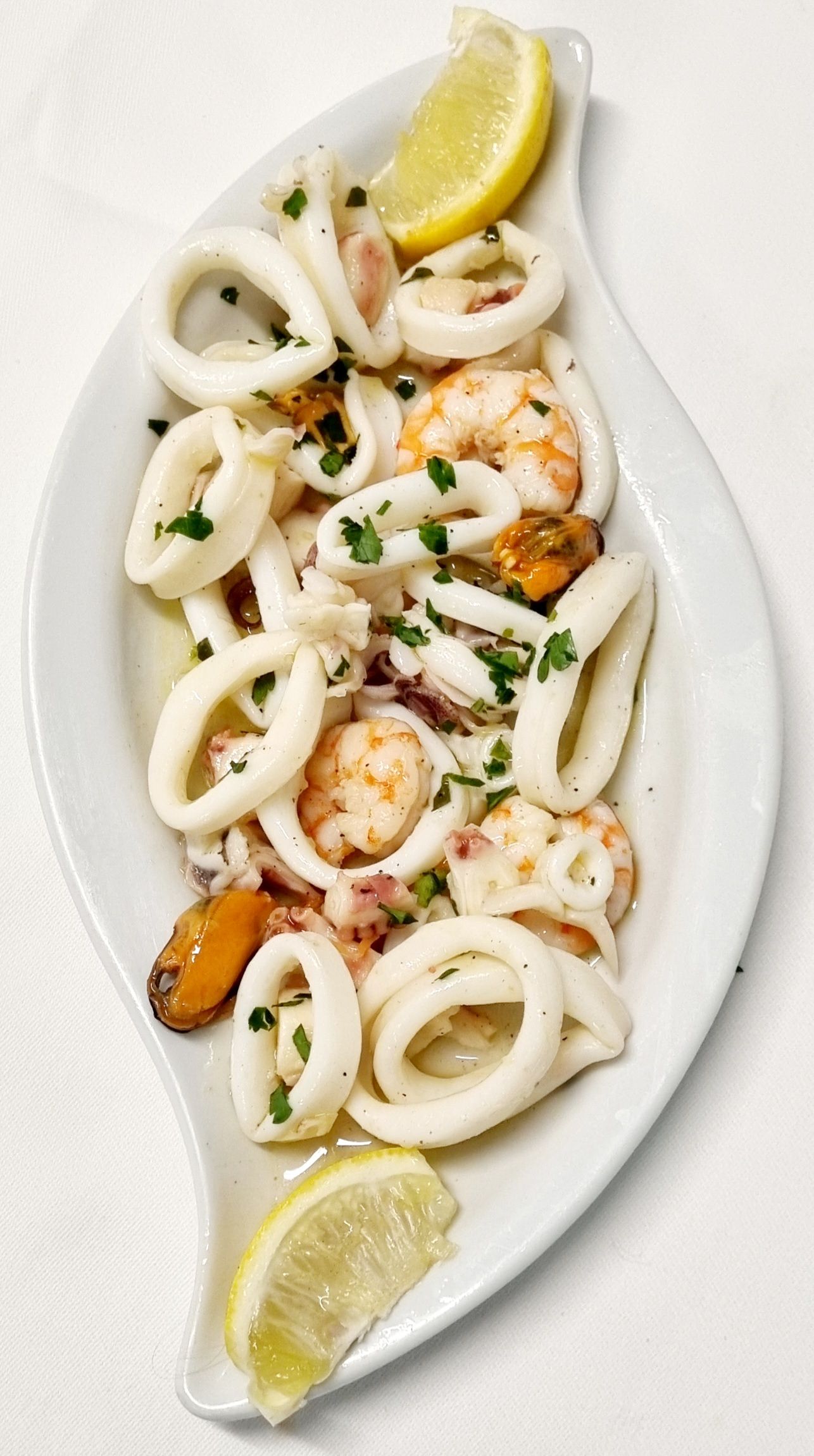 Insalata di mare con anelli di calamaro, gamberi e cozze su un piatto bianco, guarnita con limone e prezzemolo.