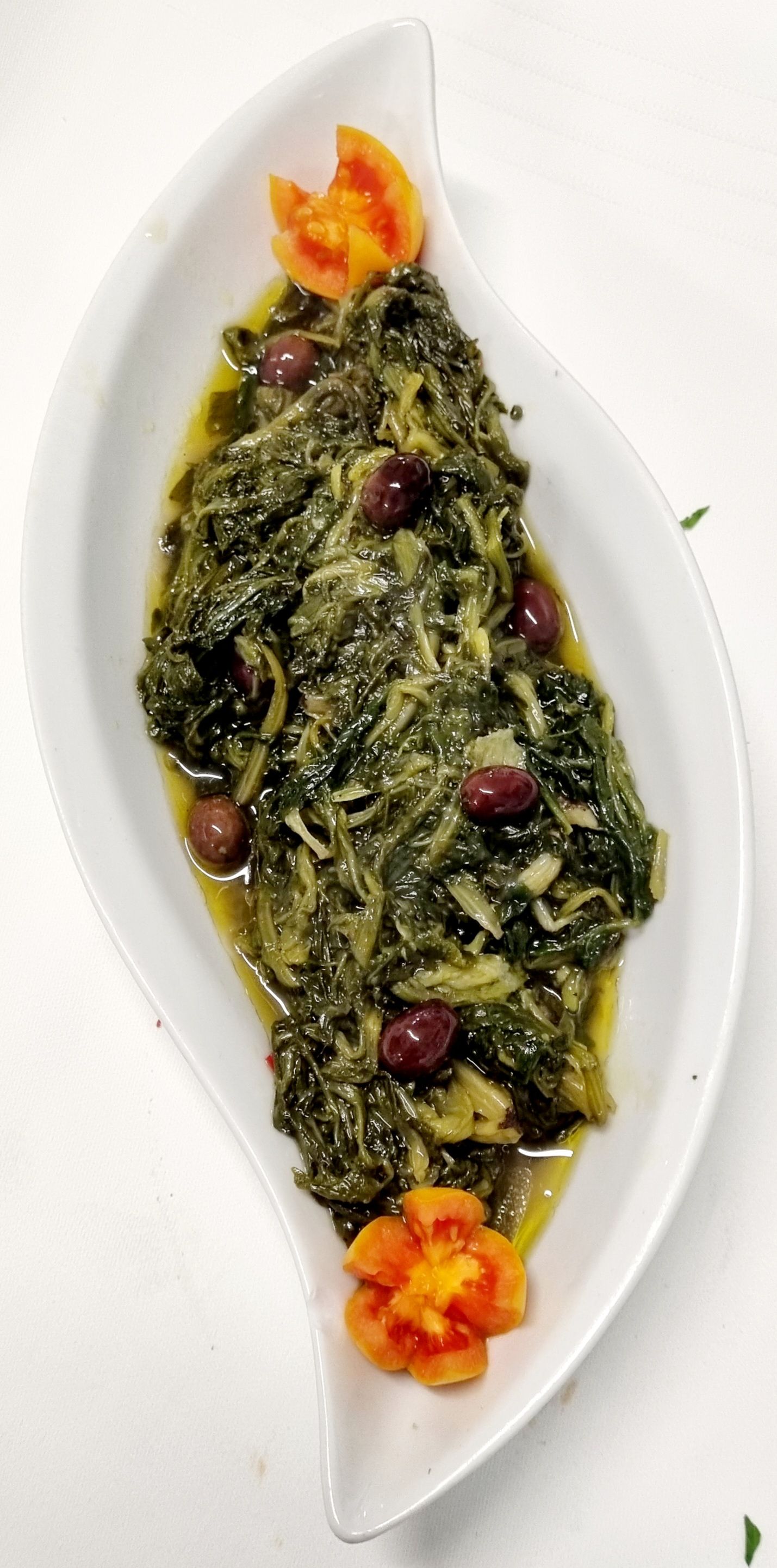 Verdure cotte di colore verde scuro con olive, servite su un piatto bianco