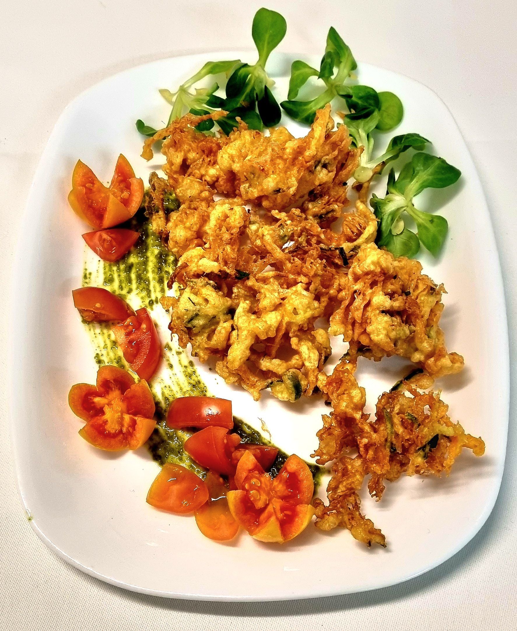 Cibo fritto su un piatto con pomodori, pesto e verdure.