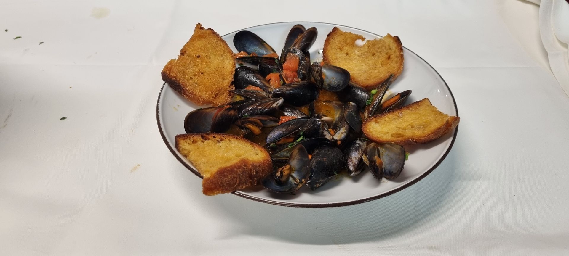 Un piatto di cozze con pane tostato su una superficie bianca.