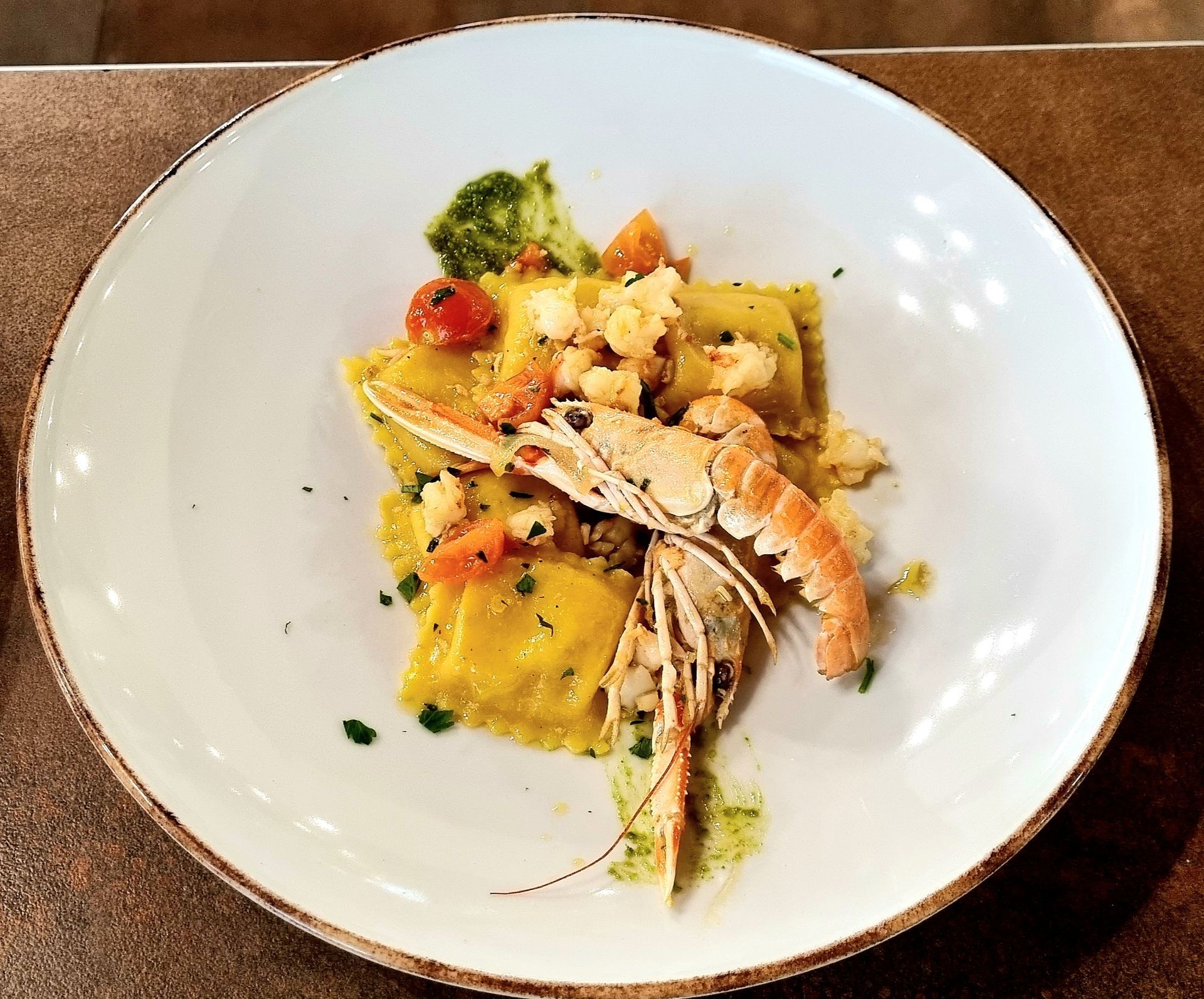 Piatto di ravioli con gamberi, pomodori e pesto.
