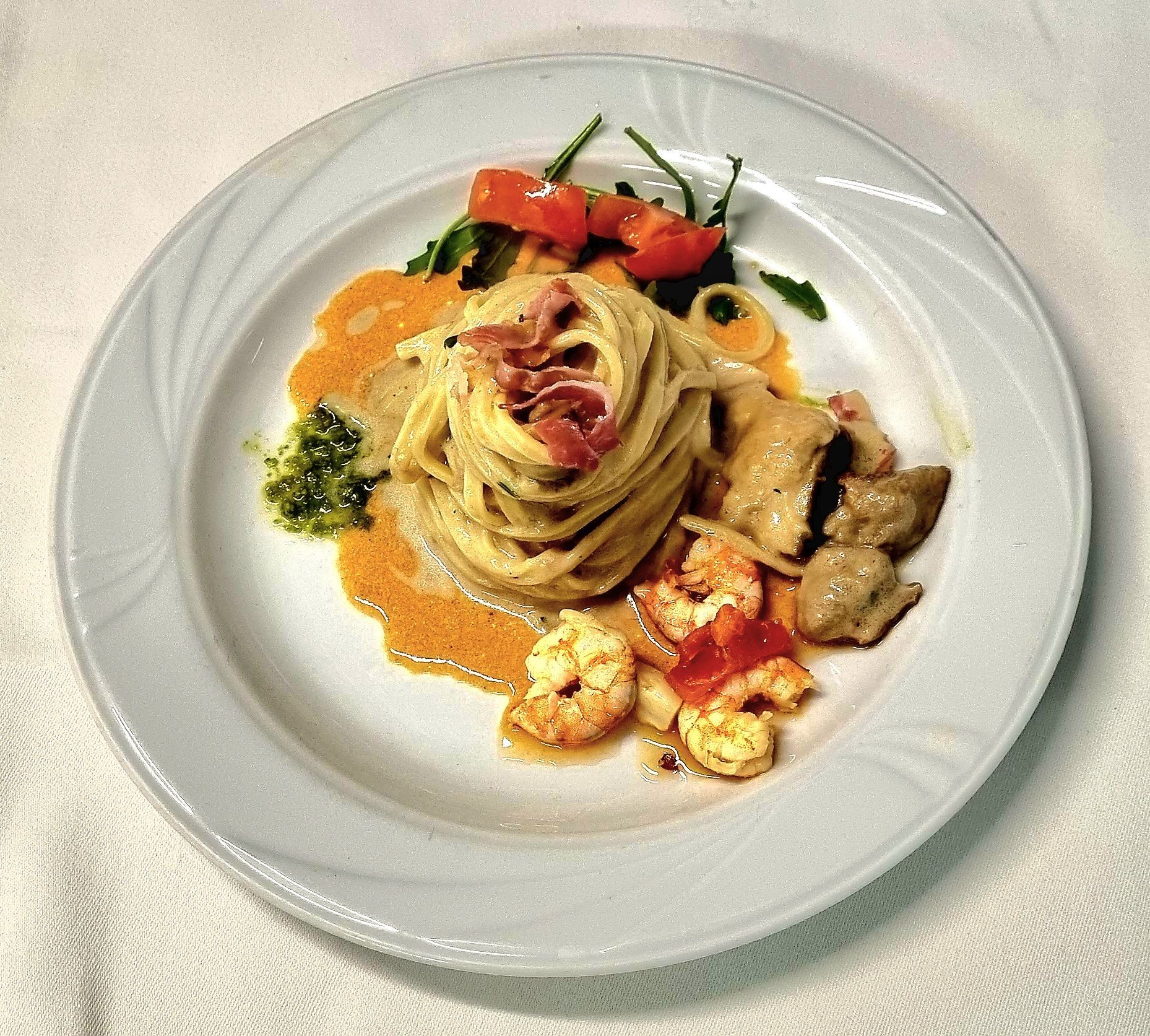 Piatto di pasta con gamberi, funghi e prosciutto, guarnito con pomodori ed erbe aromatiche.