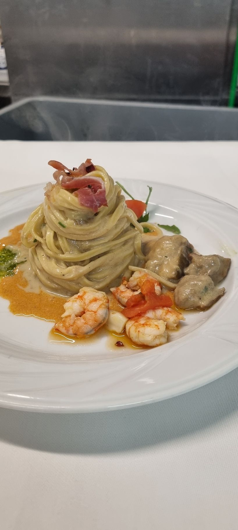 Piatto di pasta con gamberi, pomodori e prosciutto su un piatto bianco.