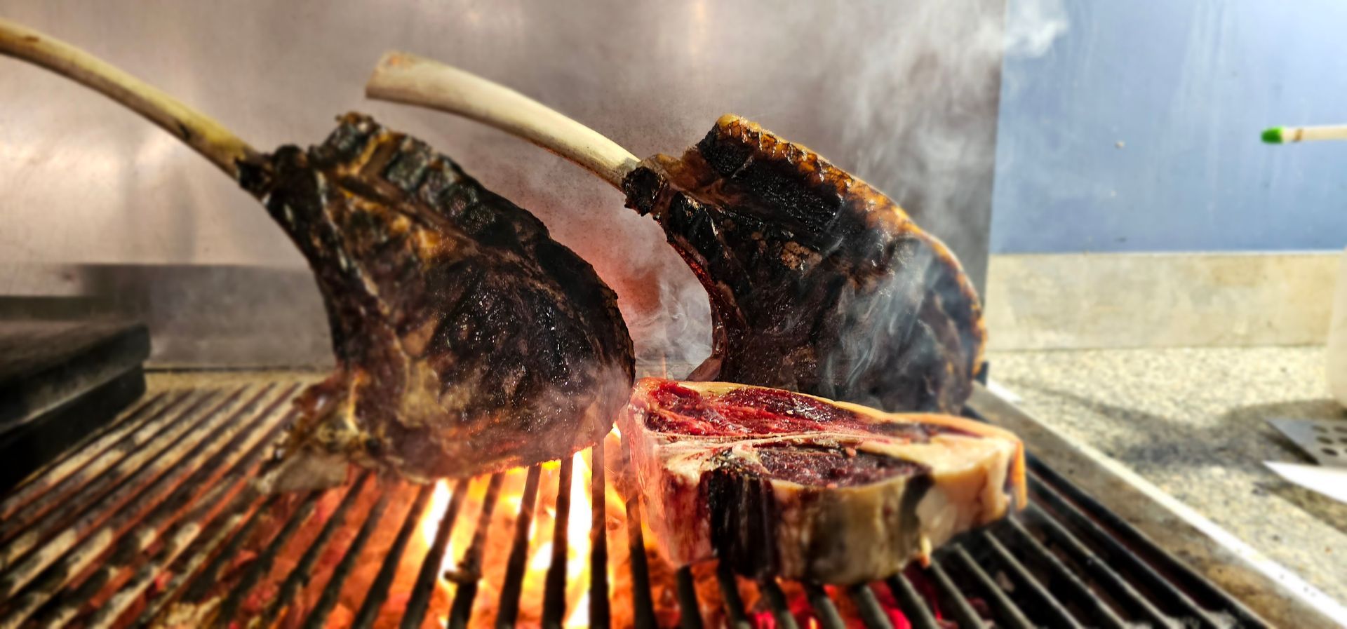 Bistecche con l'osso, cotte alla griglia su una griglia calda, con le fiamme visibili.