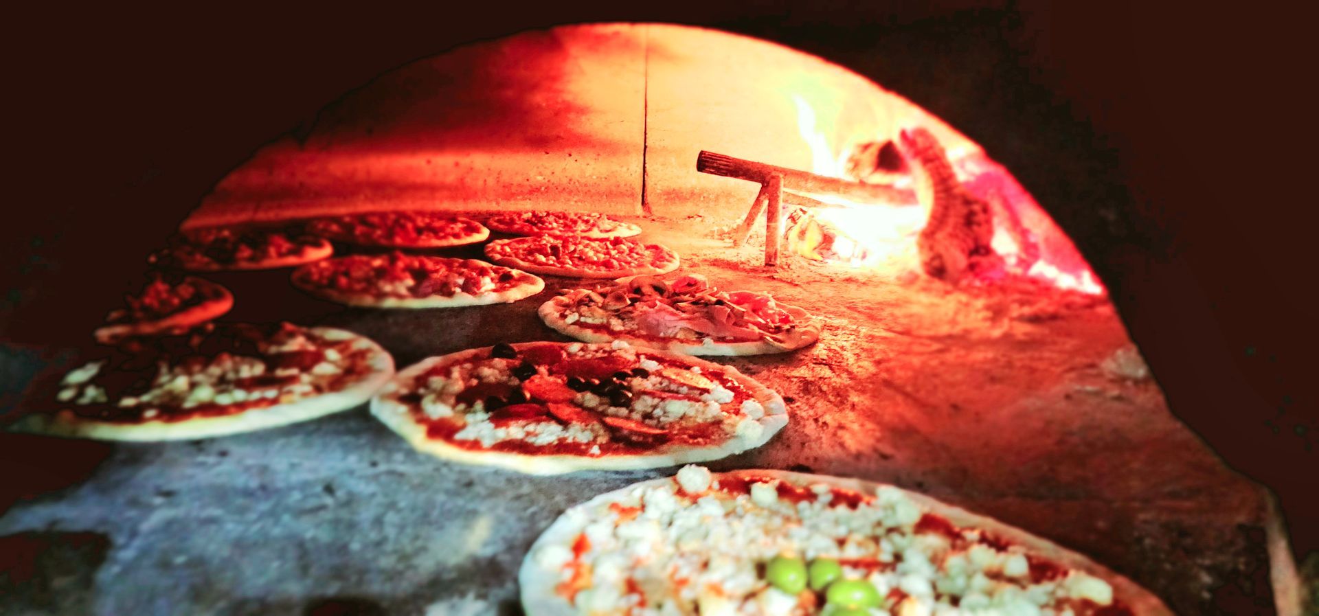 Pizze cotte nel forno a legna; luce rosso-arancio.