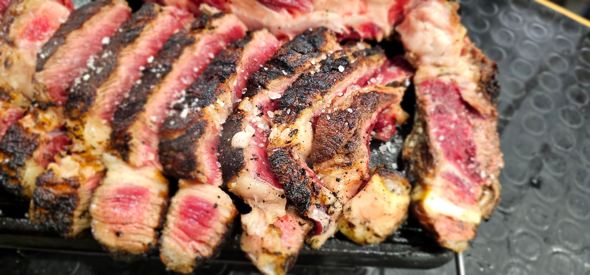 Bistecca tagliata a fette e scottata alla griglia, al sangue, con interno rosa e crosta scura, cosparsa di sale.