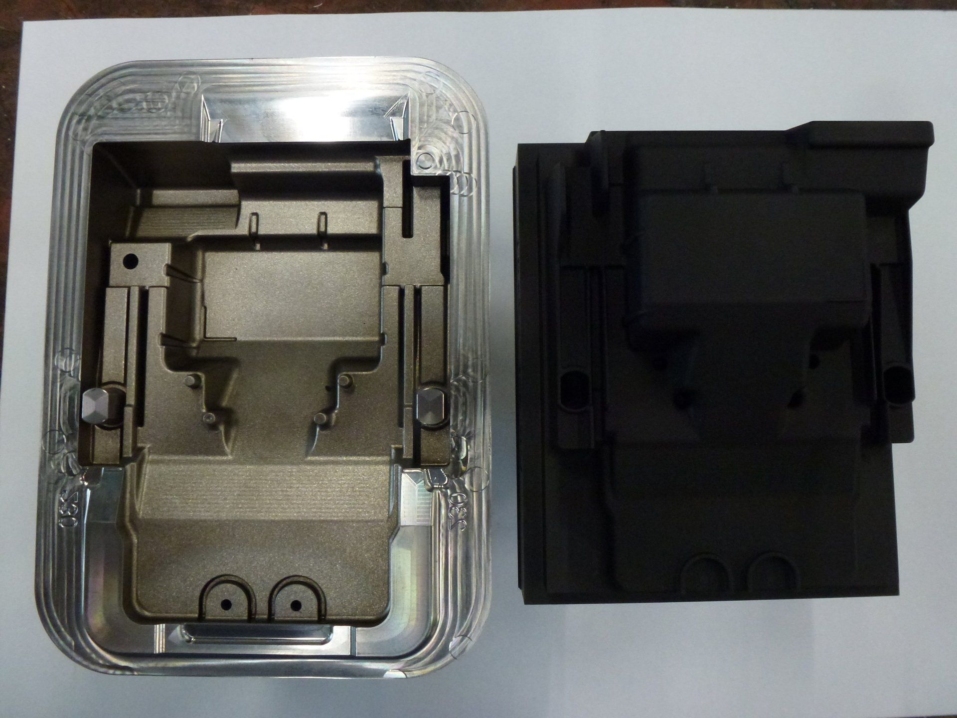 Twee stukken metaal liggen naast elkaar op een wit oppervlak.
