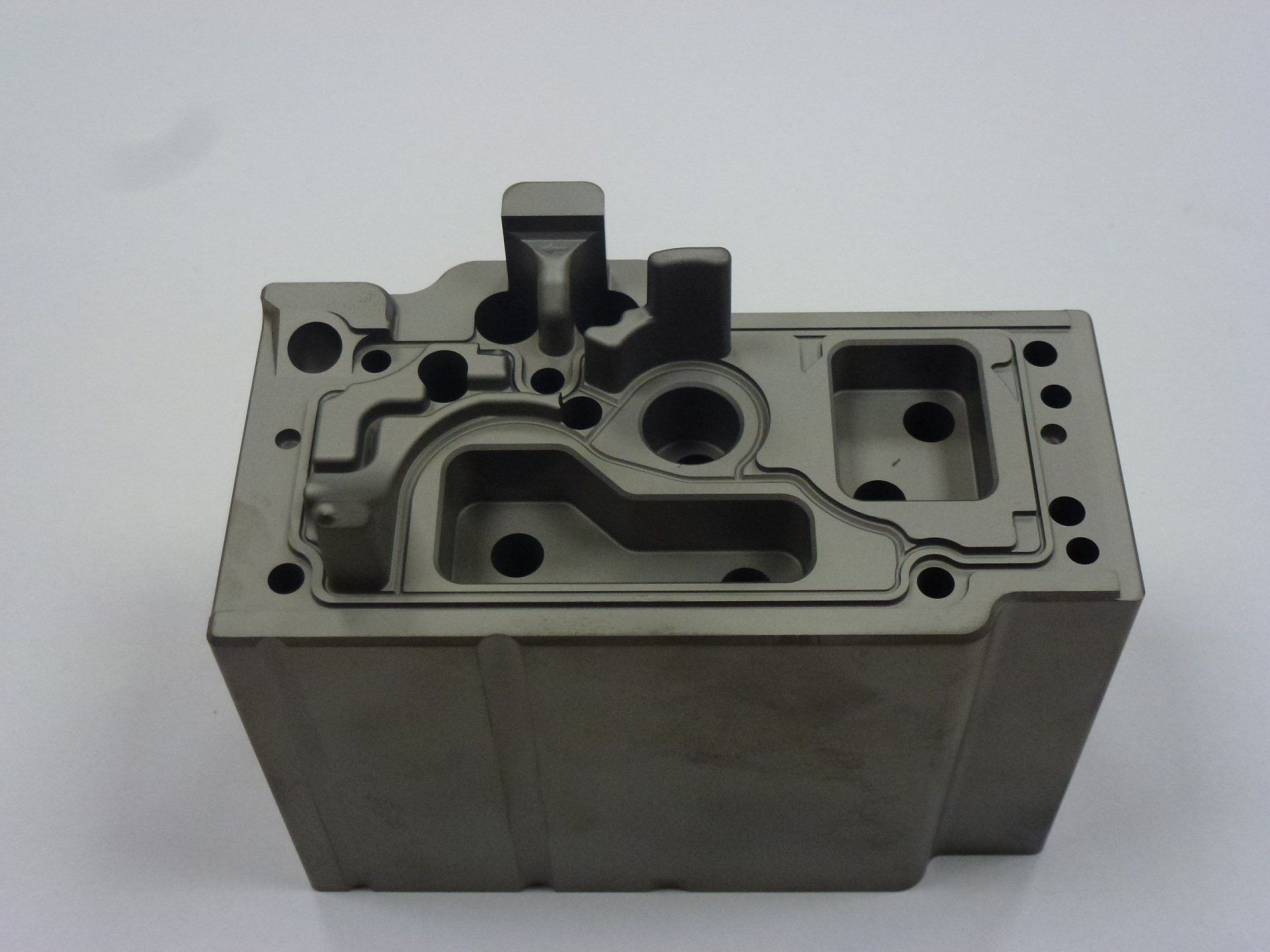 Een metalen blok met gaten erin ligt op een wit oppervlak.