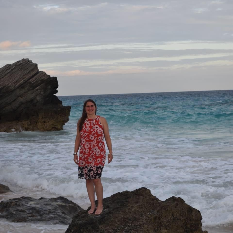 Dr. Carolina Franco in a red dress is standing on a rock near the ocean