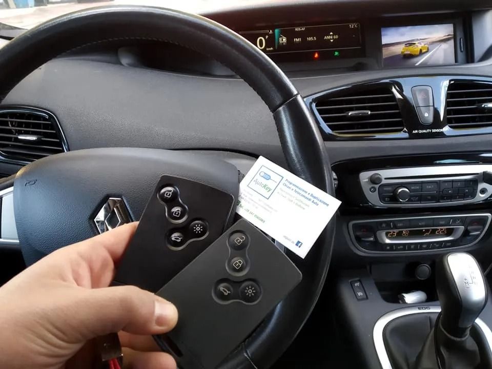 La mano di una persona che tiene due chiavi nere e una carta all'interno del volante di un'auto Renault.