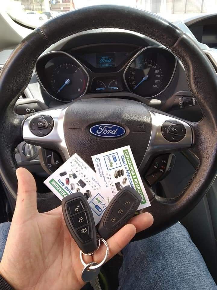 Persona che tiene in mano due chiavi dell'auto e biglietti da visita davanti al volante di una Ford.