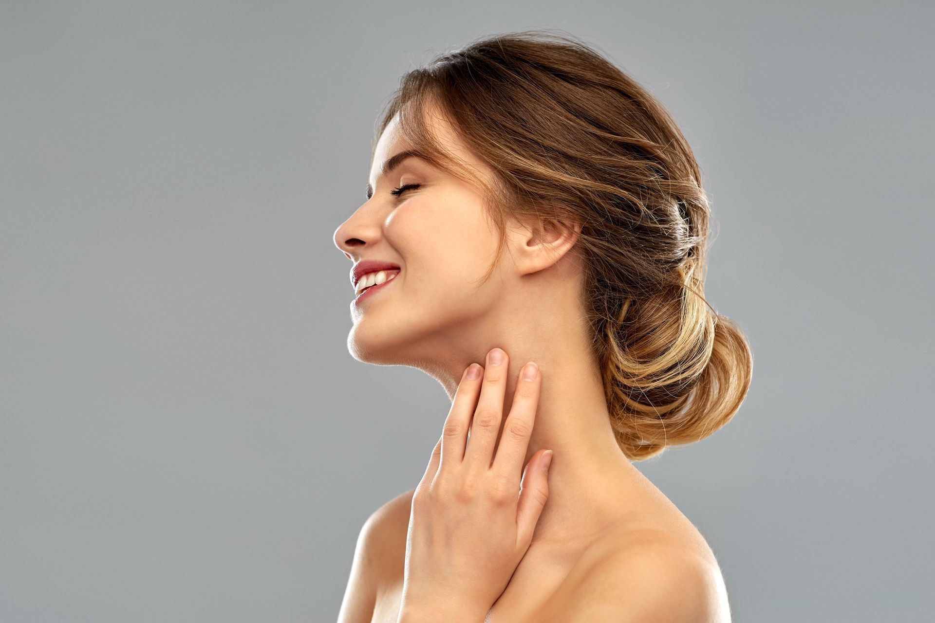 A woman is touching her neck with her hand and smiling.