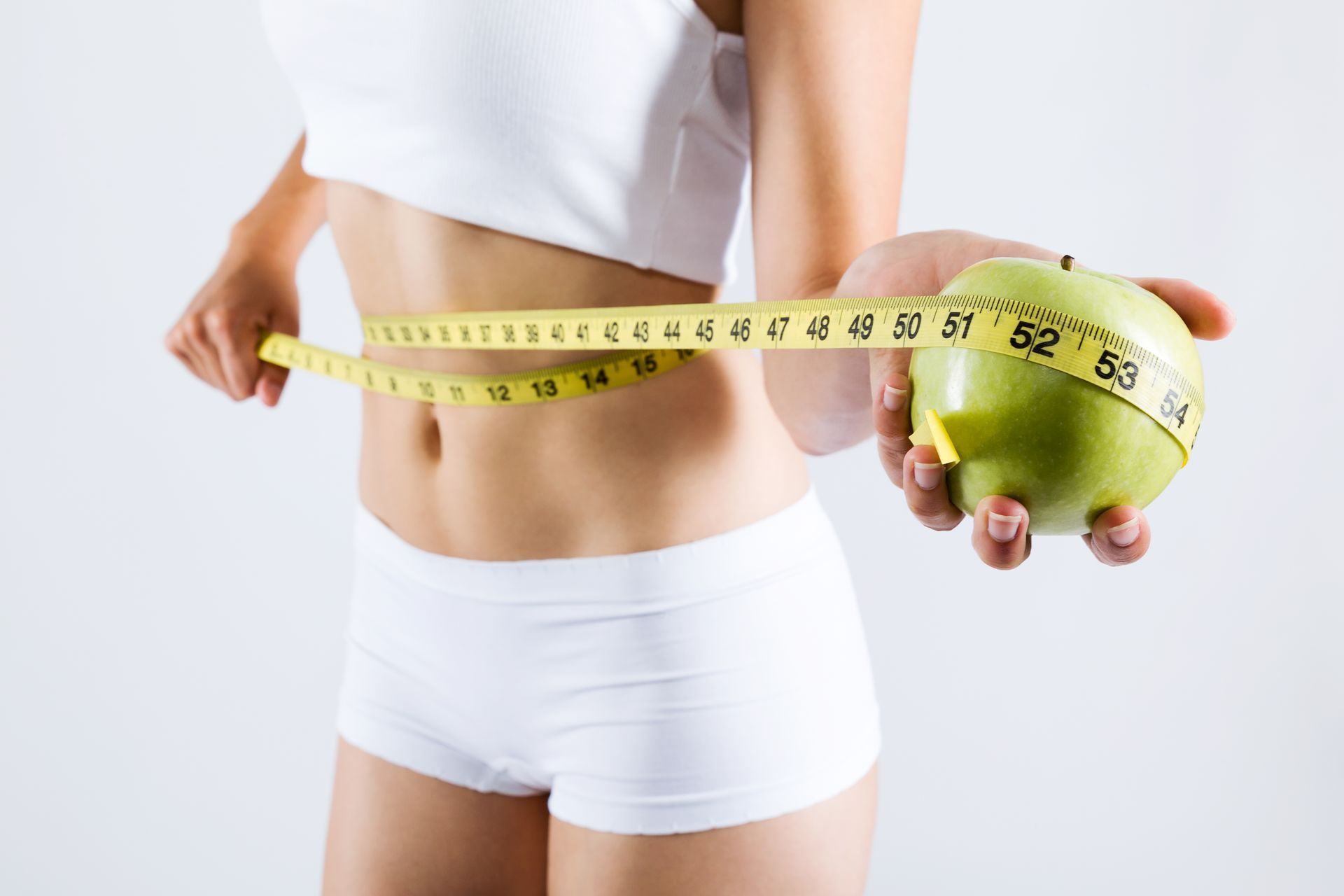 A woman is measuring her waist with a tape measure and holding an apple.