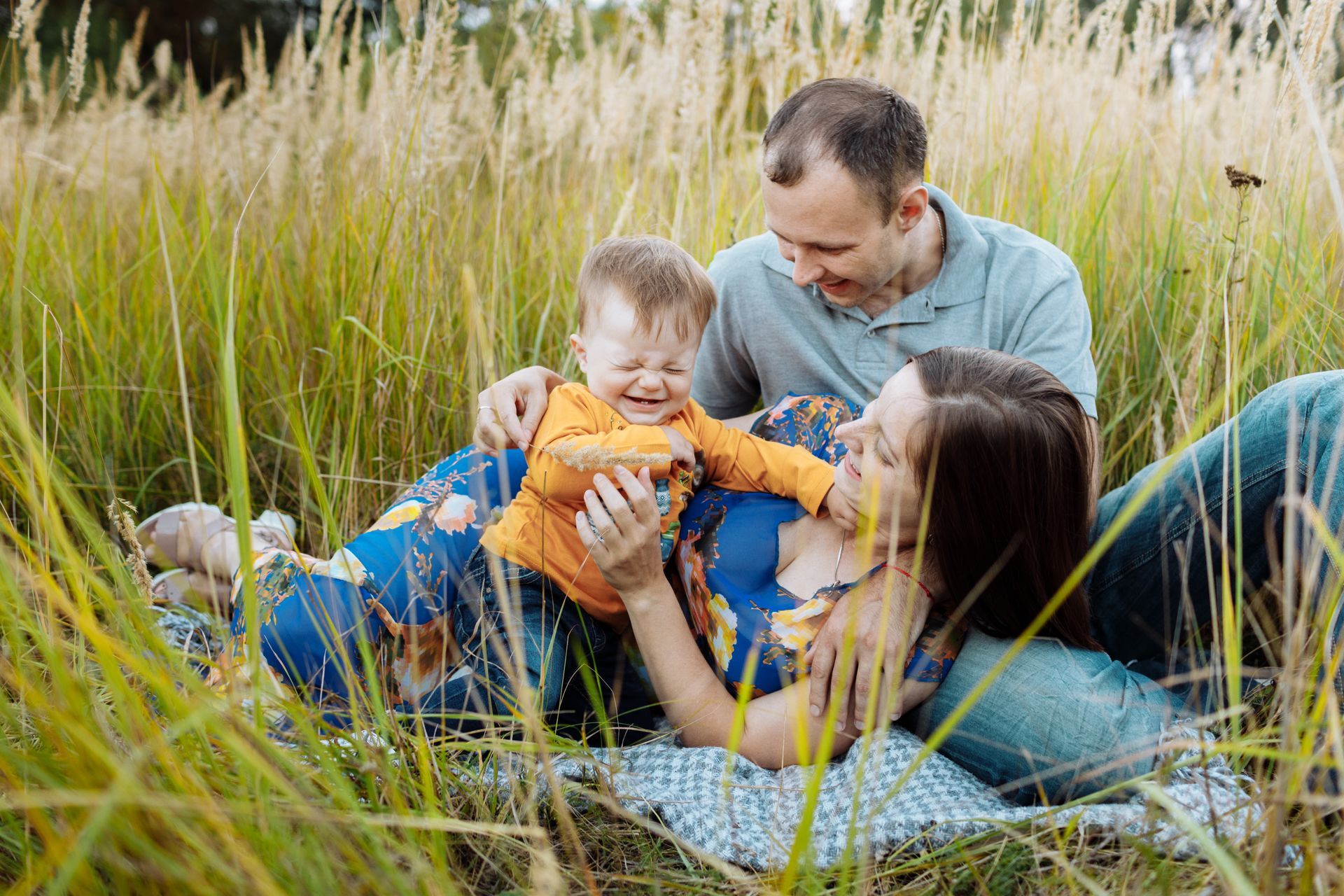 Family picnicking in tall grass, baby laughing while parents smile.