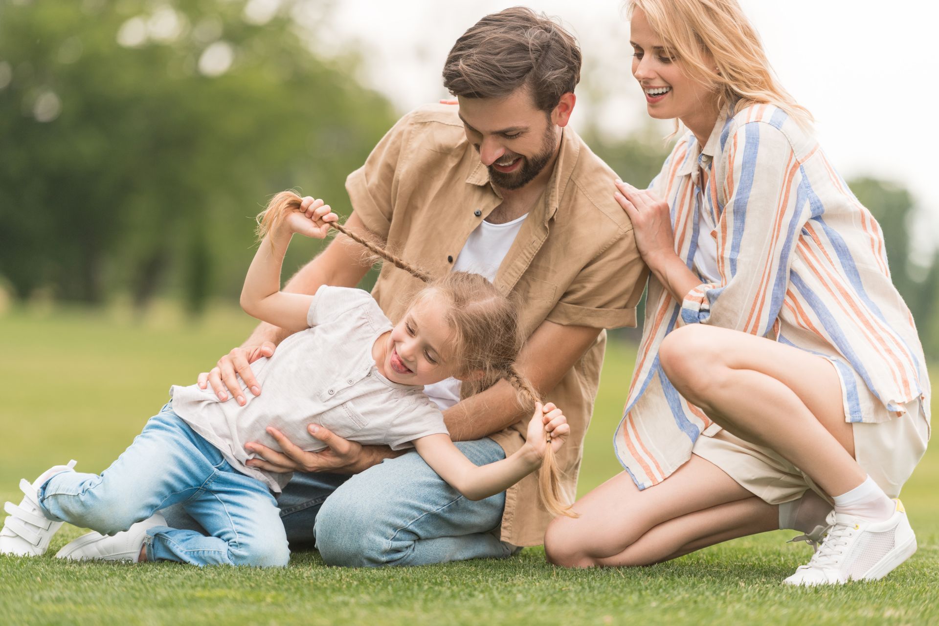 Family of four plays on green grass. Dad and daughter are interacting, while mom smiles nearby.