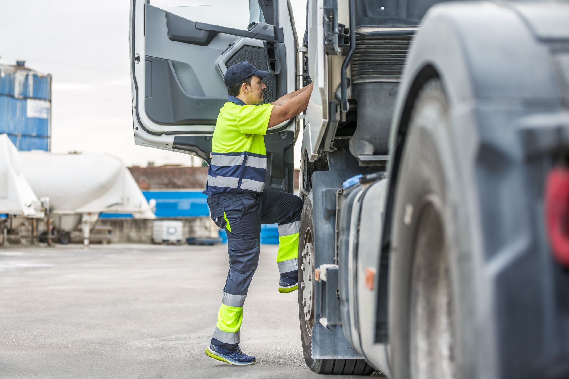 Truck driver in reflective gear climbing into a semi-truck cab.