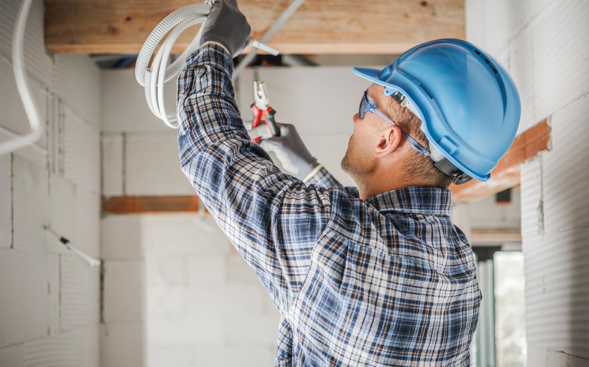 Electrician in blue hard hat working with wiring in a construction site.