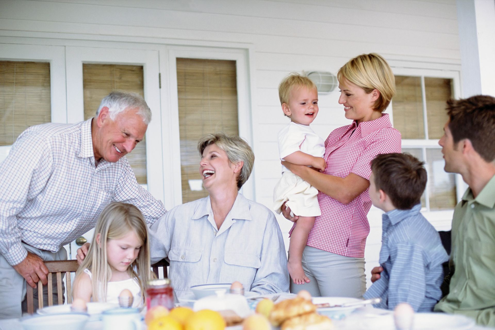 Family gathered around a table on a porch, smiling and interacting.