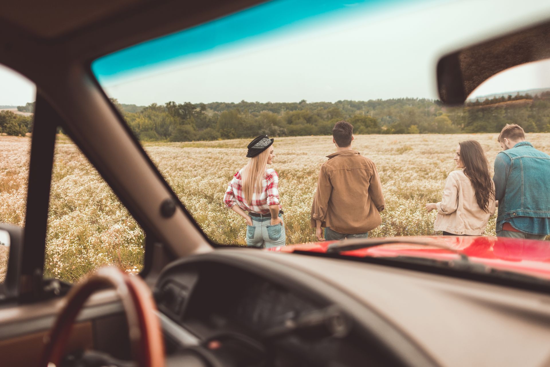 View from inside a red car of four people walking in a field of wildflowers.