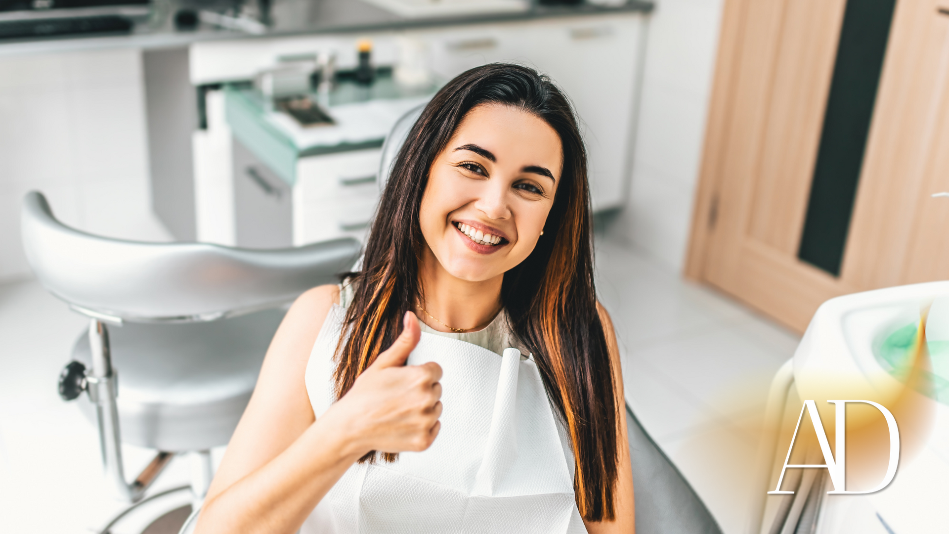 A woman is sitting in a dental chair and giving a thumbs up.