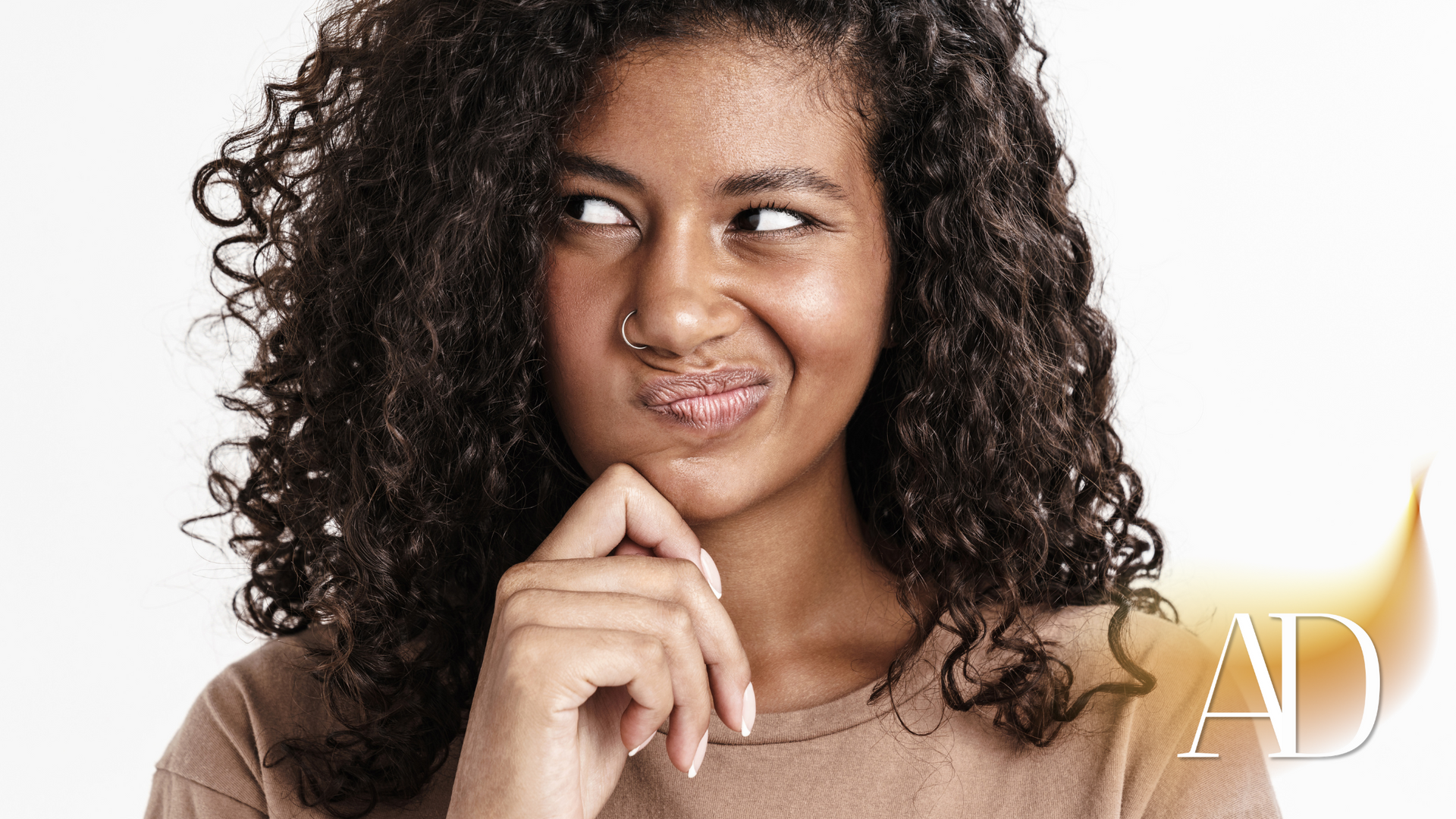 A woman with curly hair is smiling with her hand on her chin.