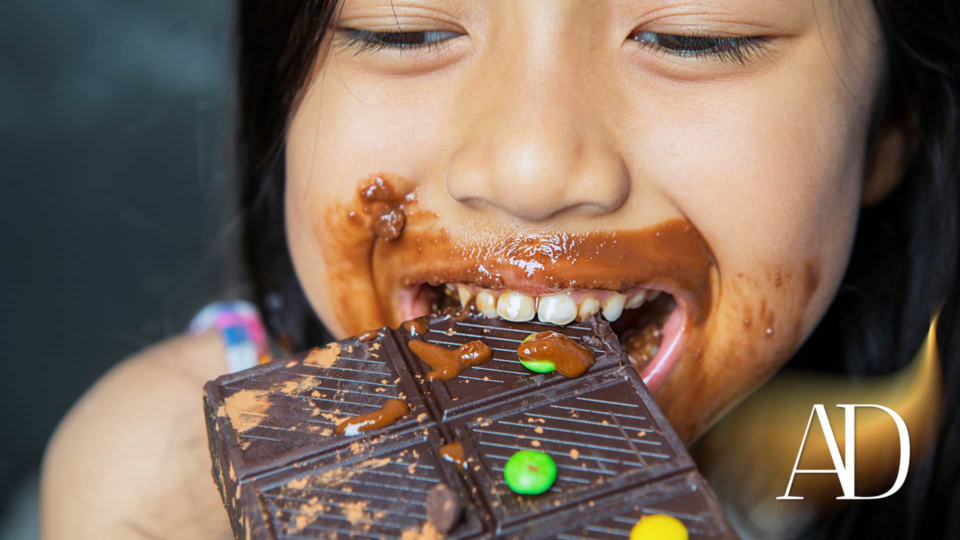 Girl eating chocolate bar, chocolate smeared around her mouth, smiling.